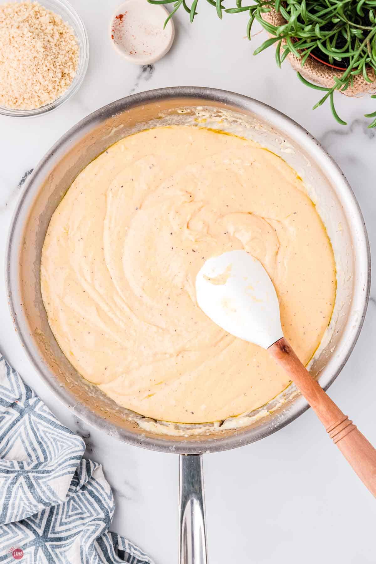 skillet with cheese sauce being stirred with white spatula