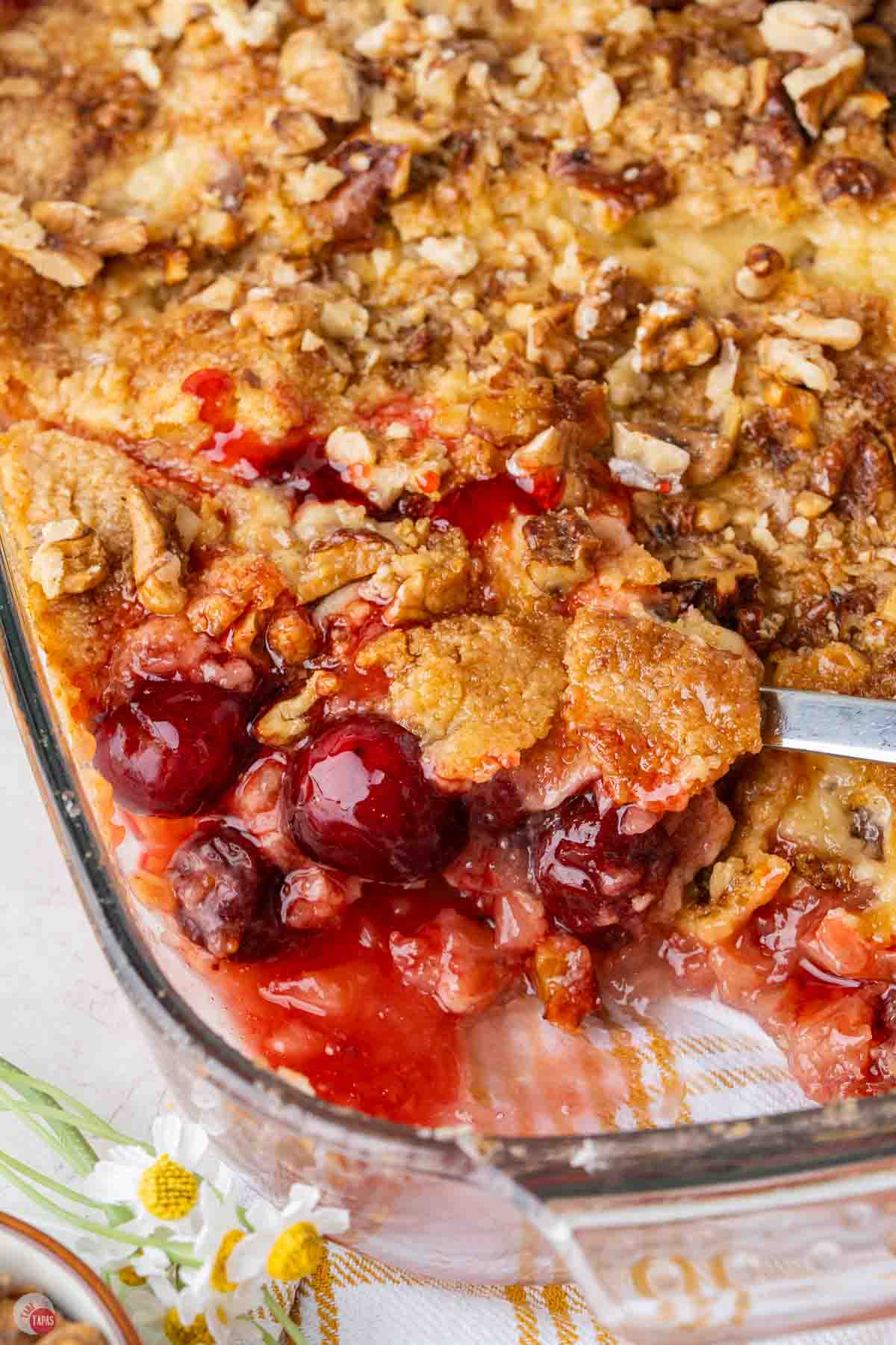 cherry dump cake in a clear baking dish with a spoon scooping some out