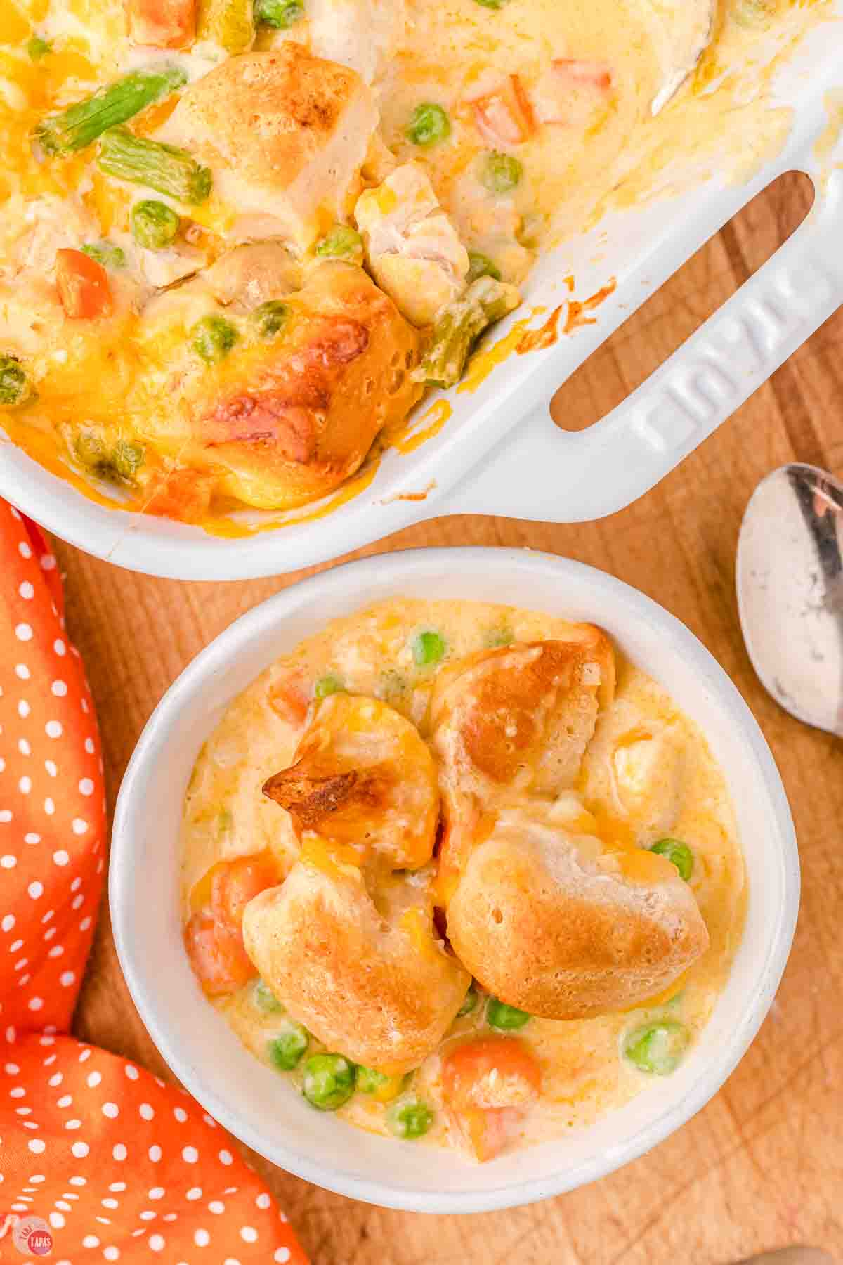 bowl of chicken bubble up casserole next to a dish and an orange napkin