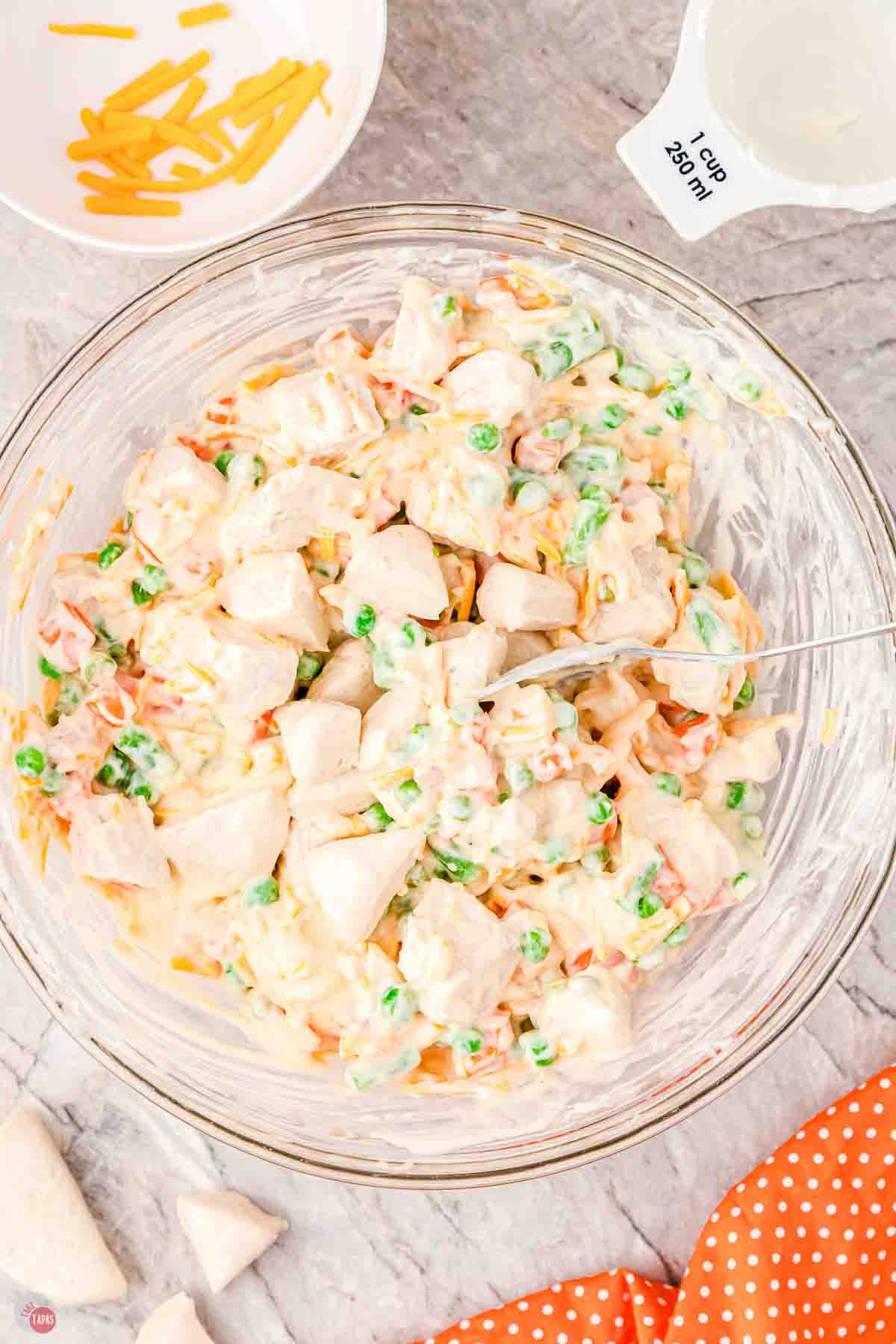 clear bowl with chicken, vegetables, and biscuits being mixed together