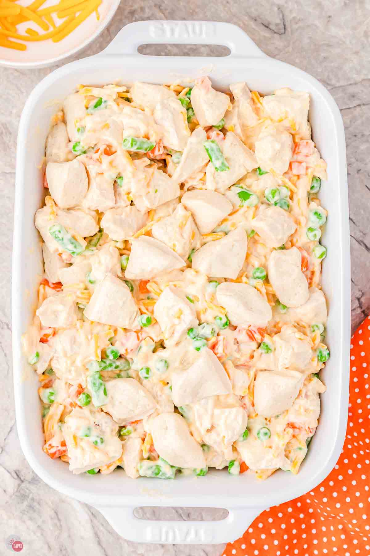 white casserole dish with chicken, vegetables, cheese, and topped with cut canned biscuits