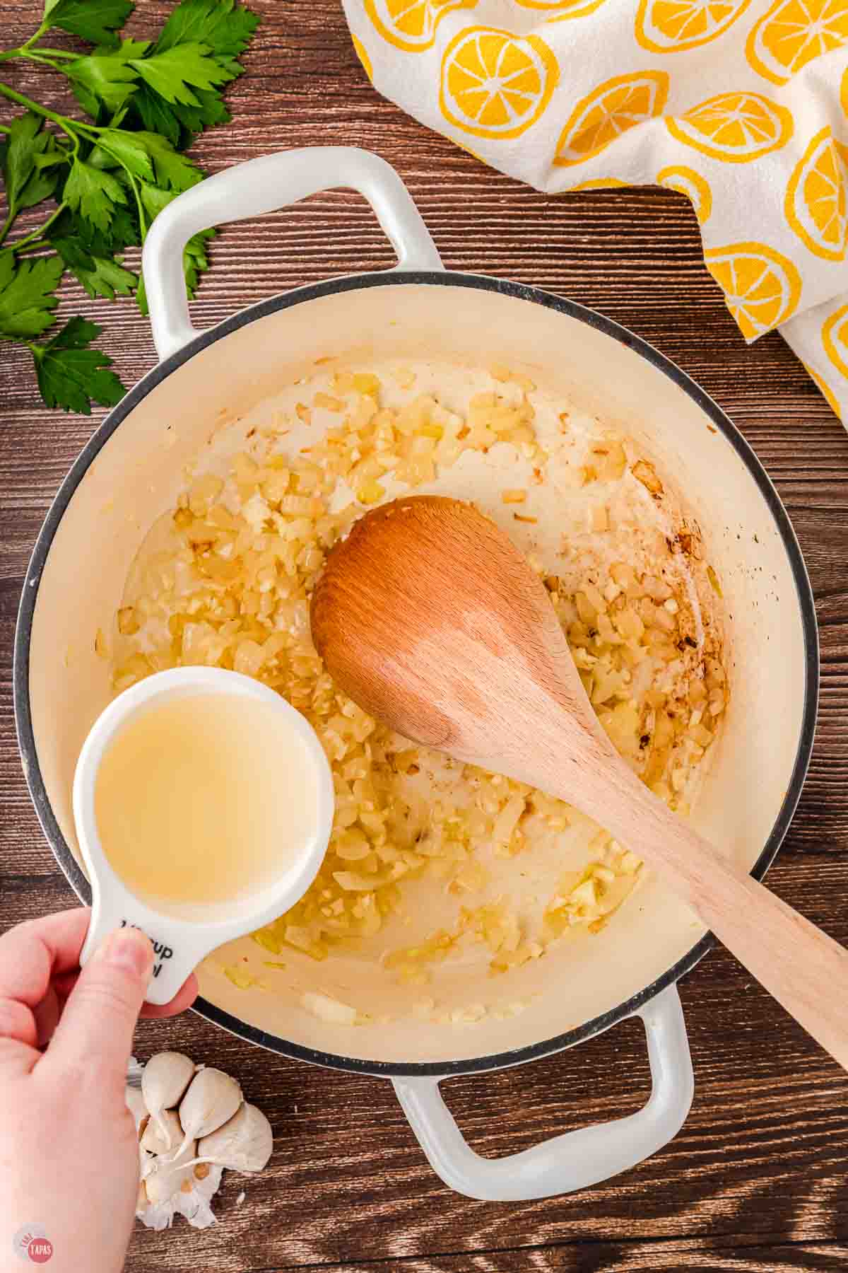 white pot with wood spoon stirring diced onion