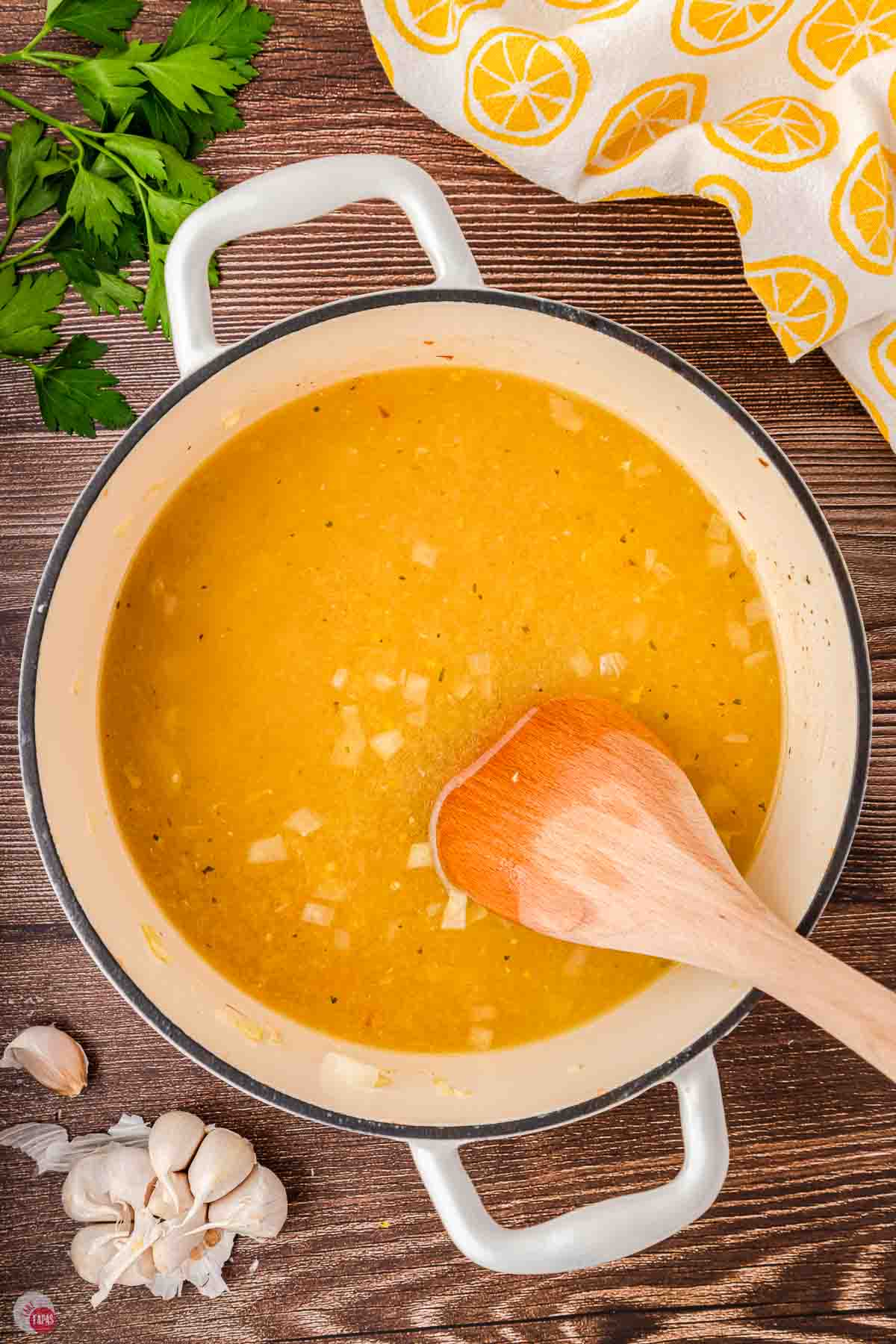 chicken broth in a pot being stirred with a wood spoon