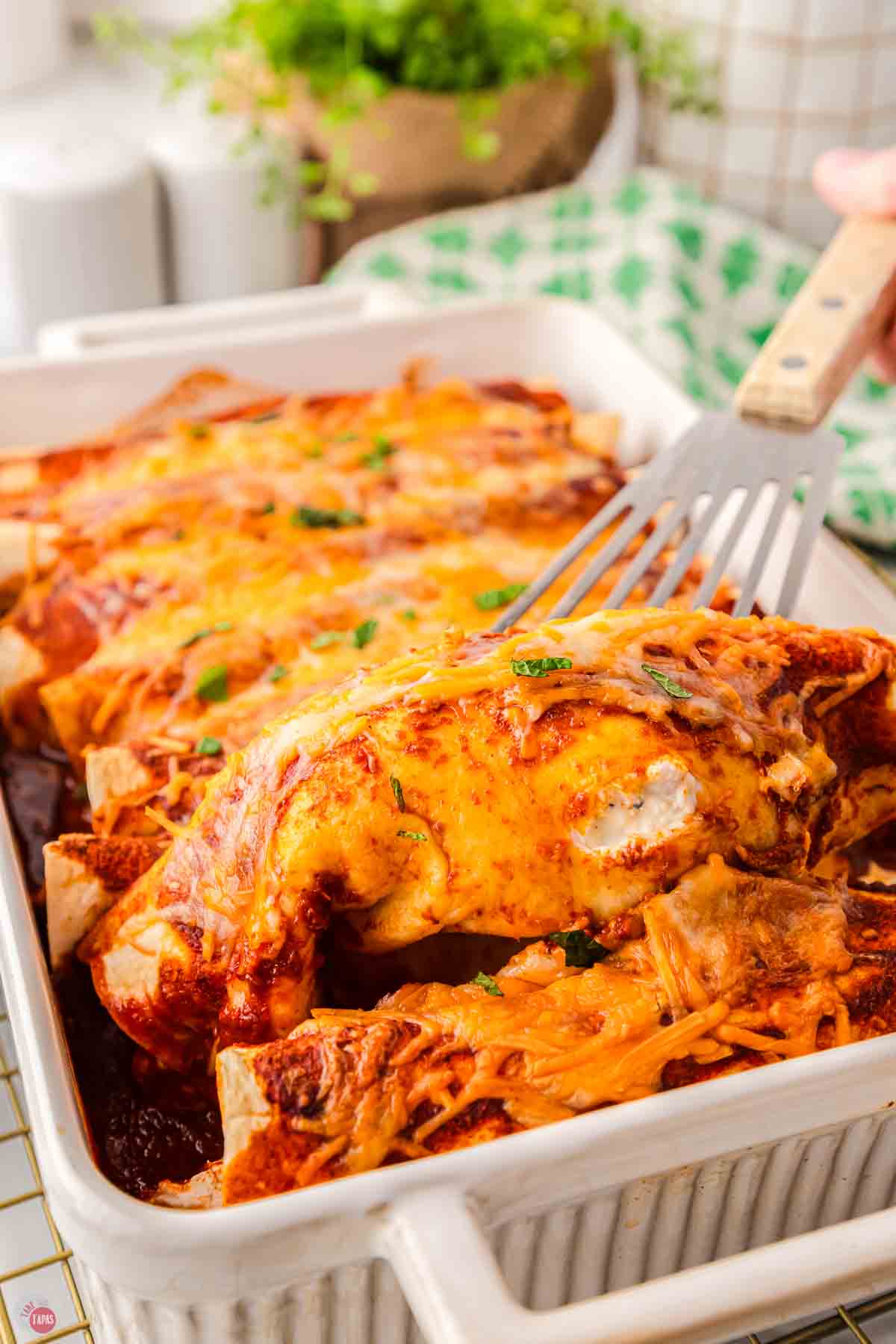 spatula lifting an enchilada out of a baking dish