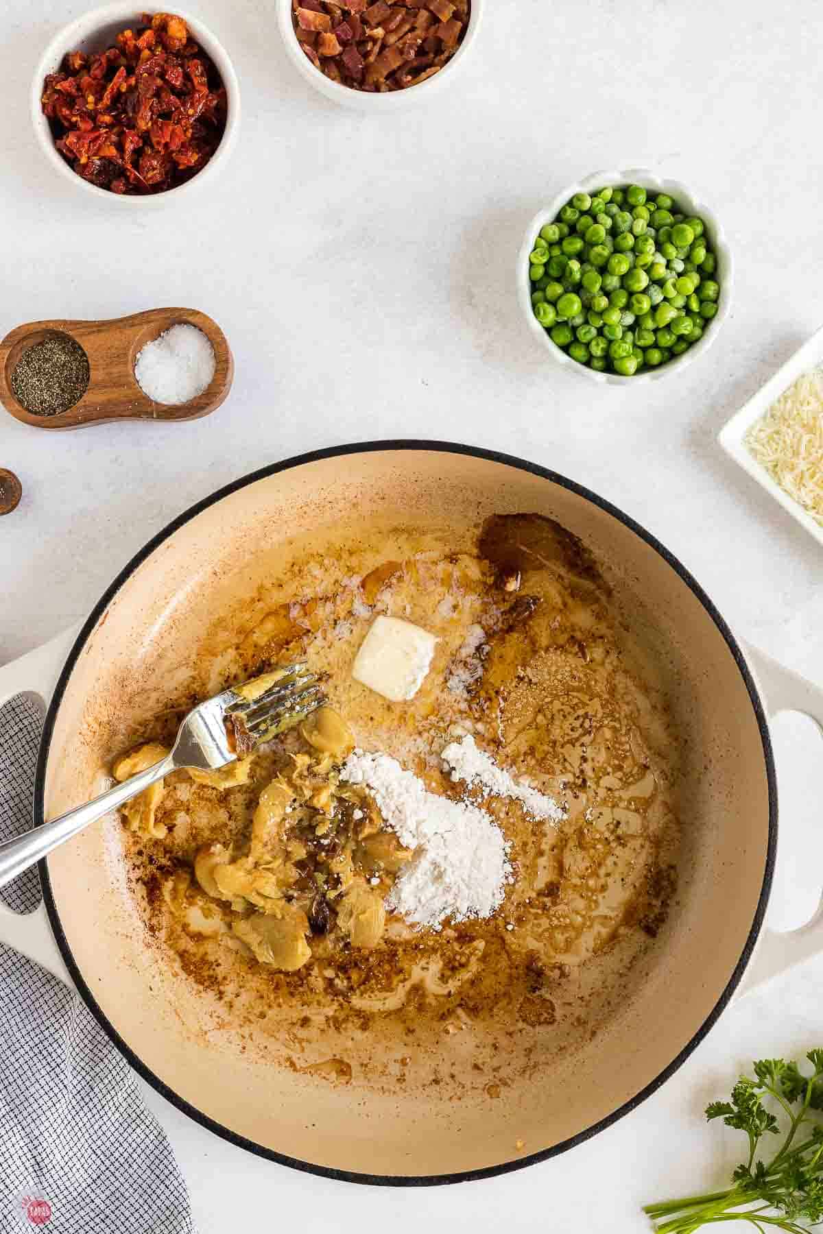 white skillet with roasted garlic, flour, and butter being stirred together