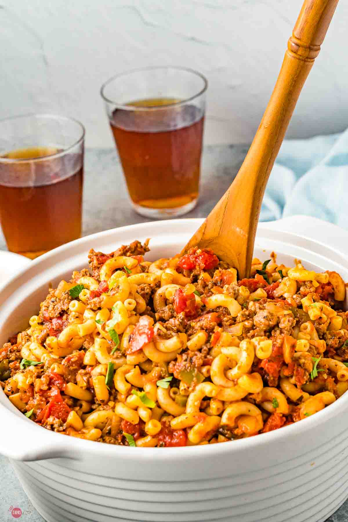 white pot of goulash with a wood spoon and two glasses of iced tea