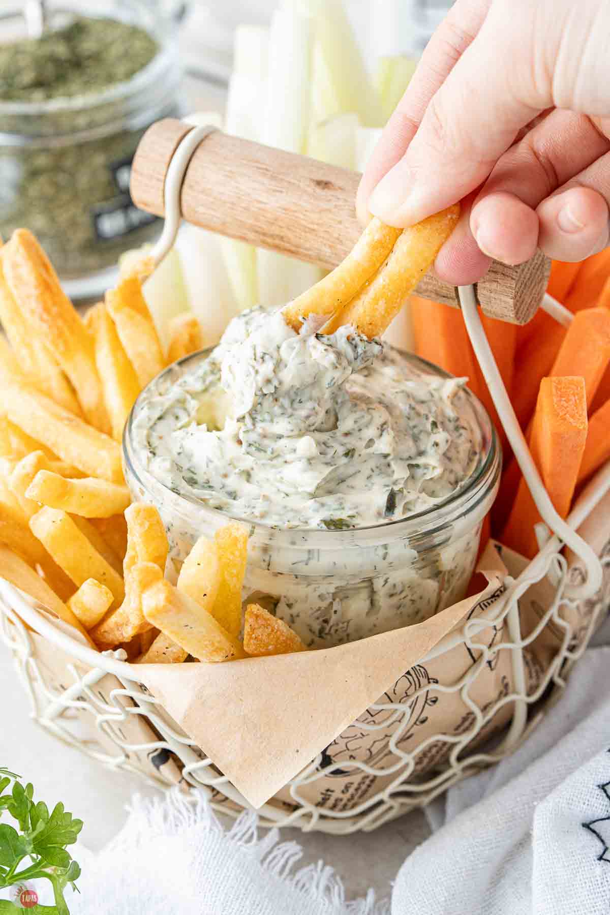 hand using french fries to dip ranch dip out of a glass jar