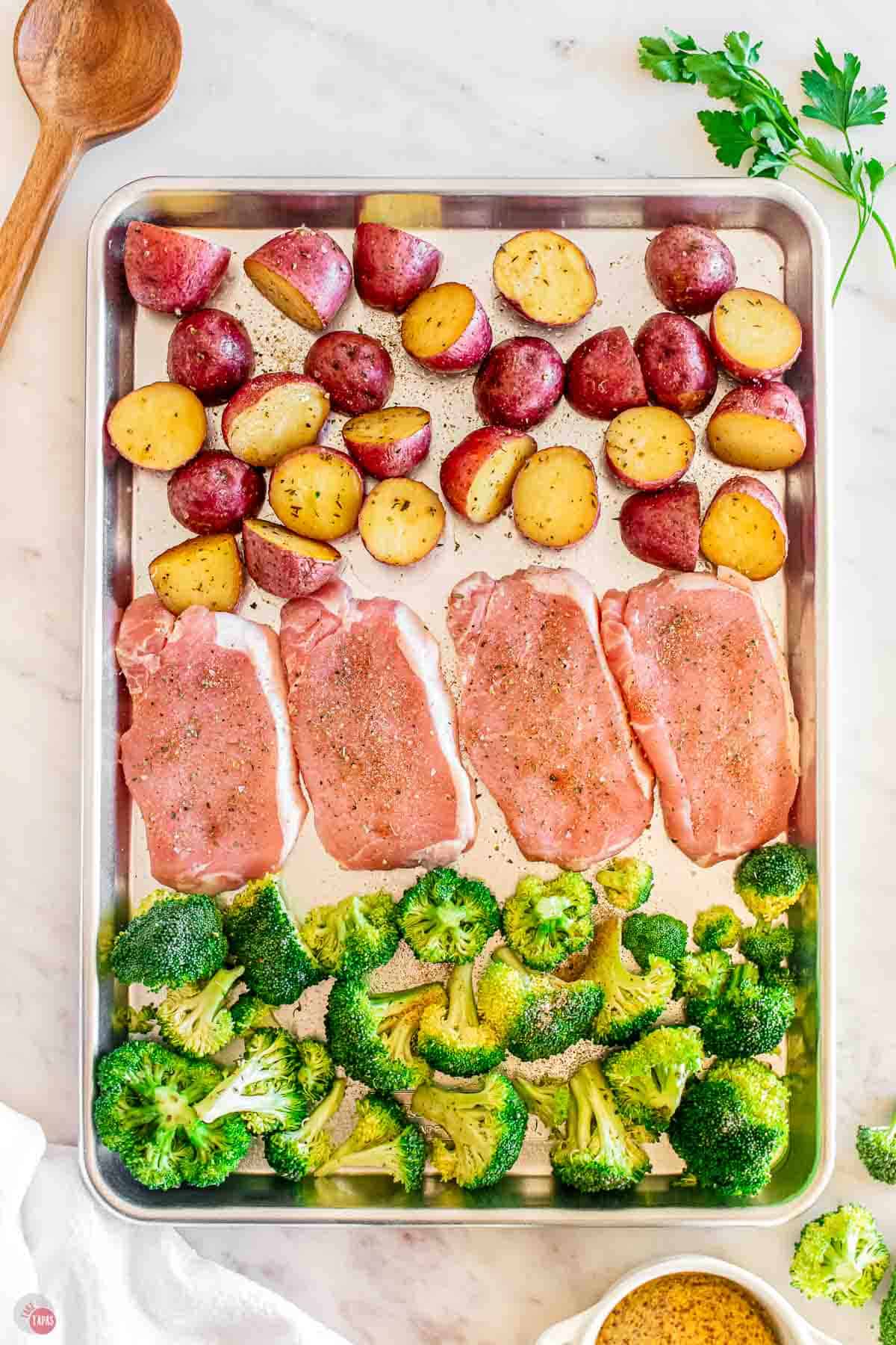 baking sheet with pork chops, broccoli, and red potatoes laid out in rows