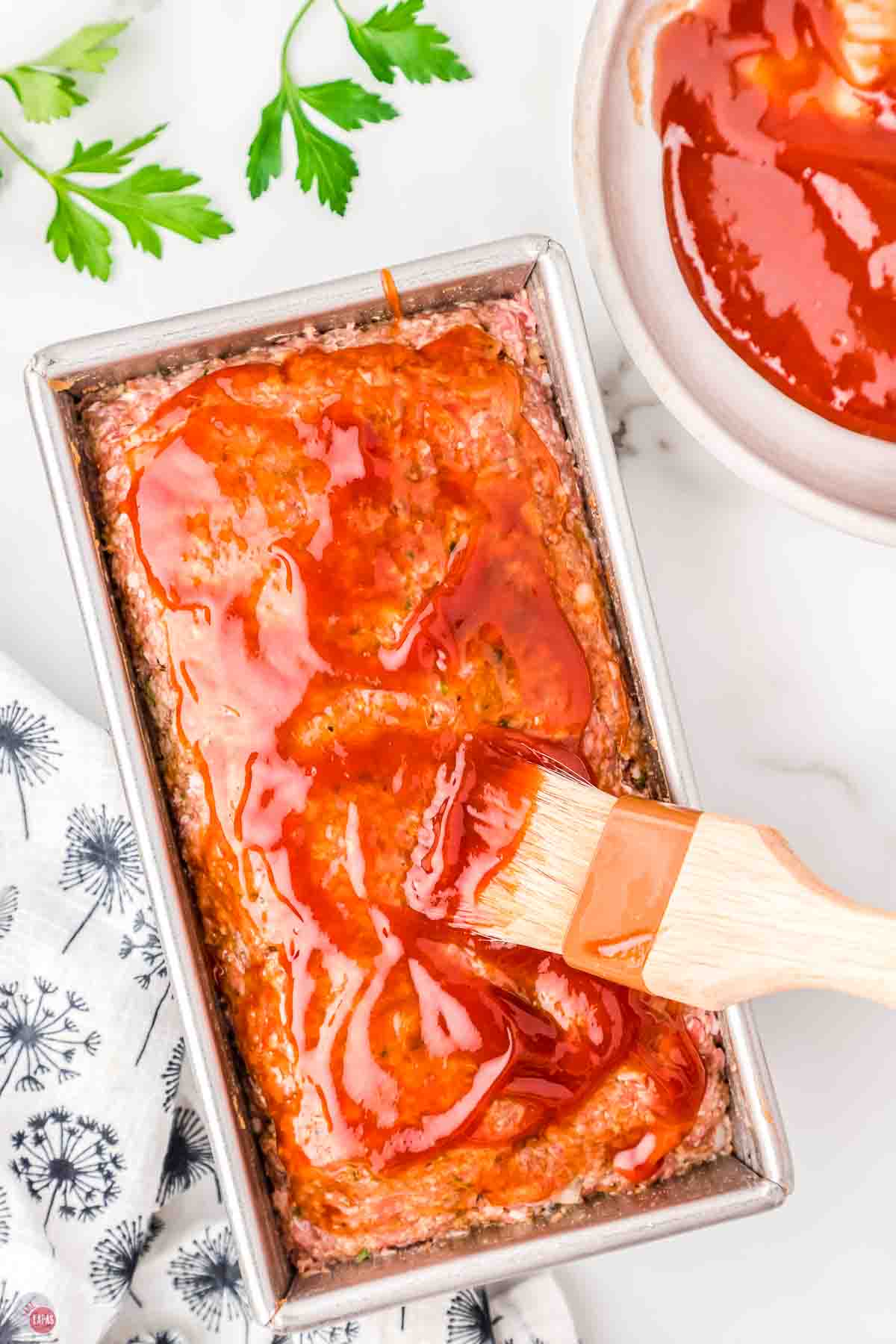 unbaked meatloaf in a loaf pan being brushed with sauce