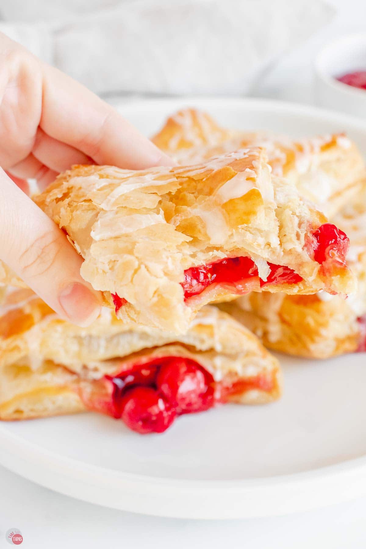 hand holding a cherry turnover with a bite missing