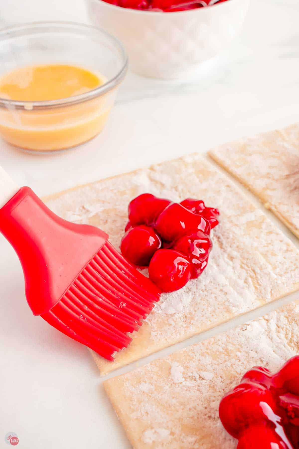 red silicone pastry brush putting egg wash on a pieces of parchment paper