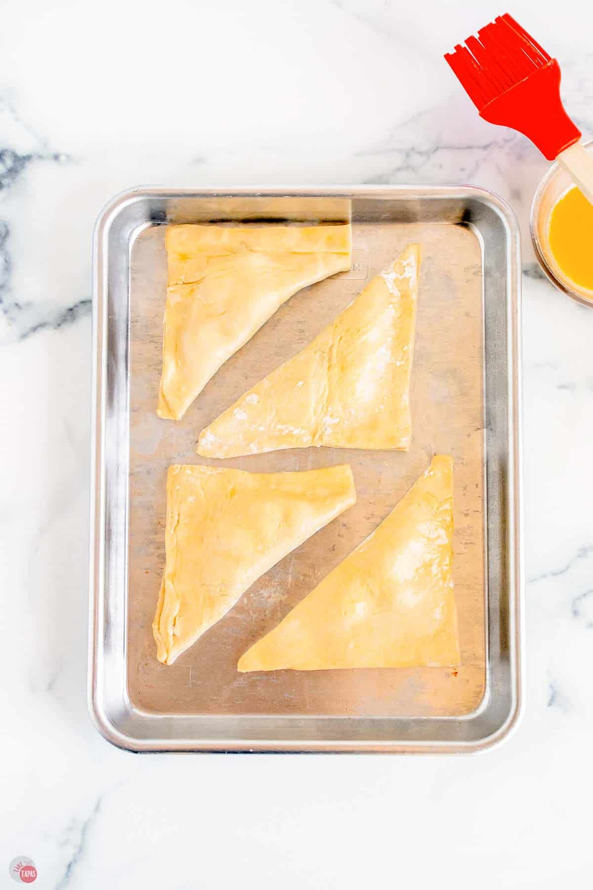 unbaked turnovers on a metal baking sheet topped with egg wash
