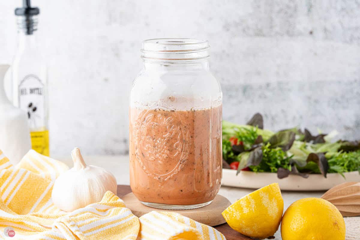 jar of homemade red wine vinaigrette dressing on a wood board with lemons in front of it