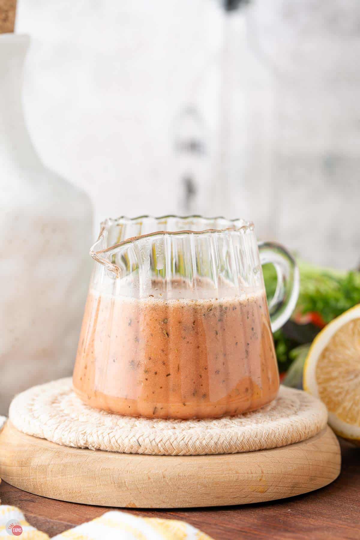 small jar with a handle full of red wine vinaigrette dressing sitting on a wood board