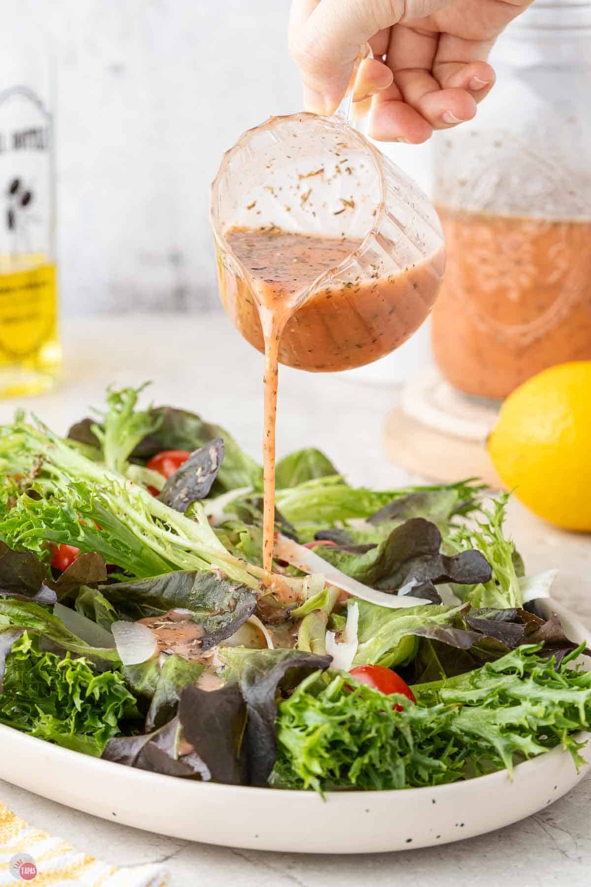 salad dressing being poured over a plate of salad greens
