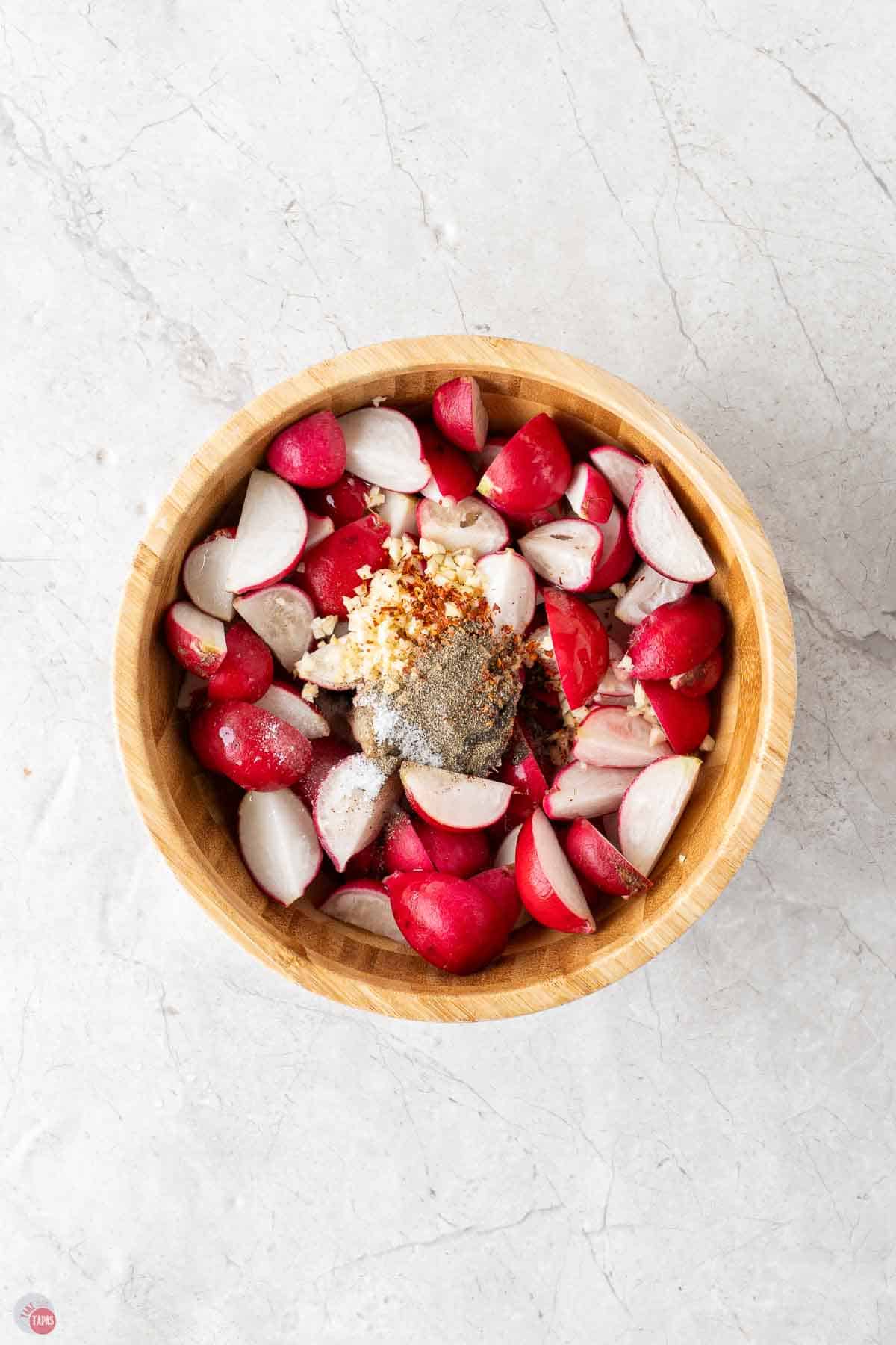 cut radishes in a wood bowl with spices and garlic on top