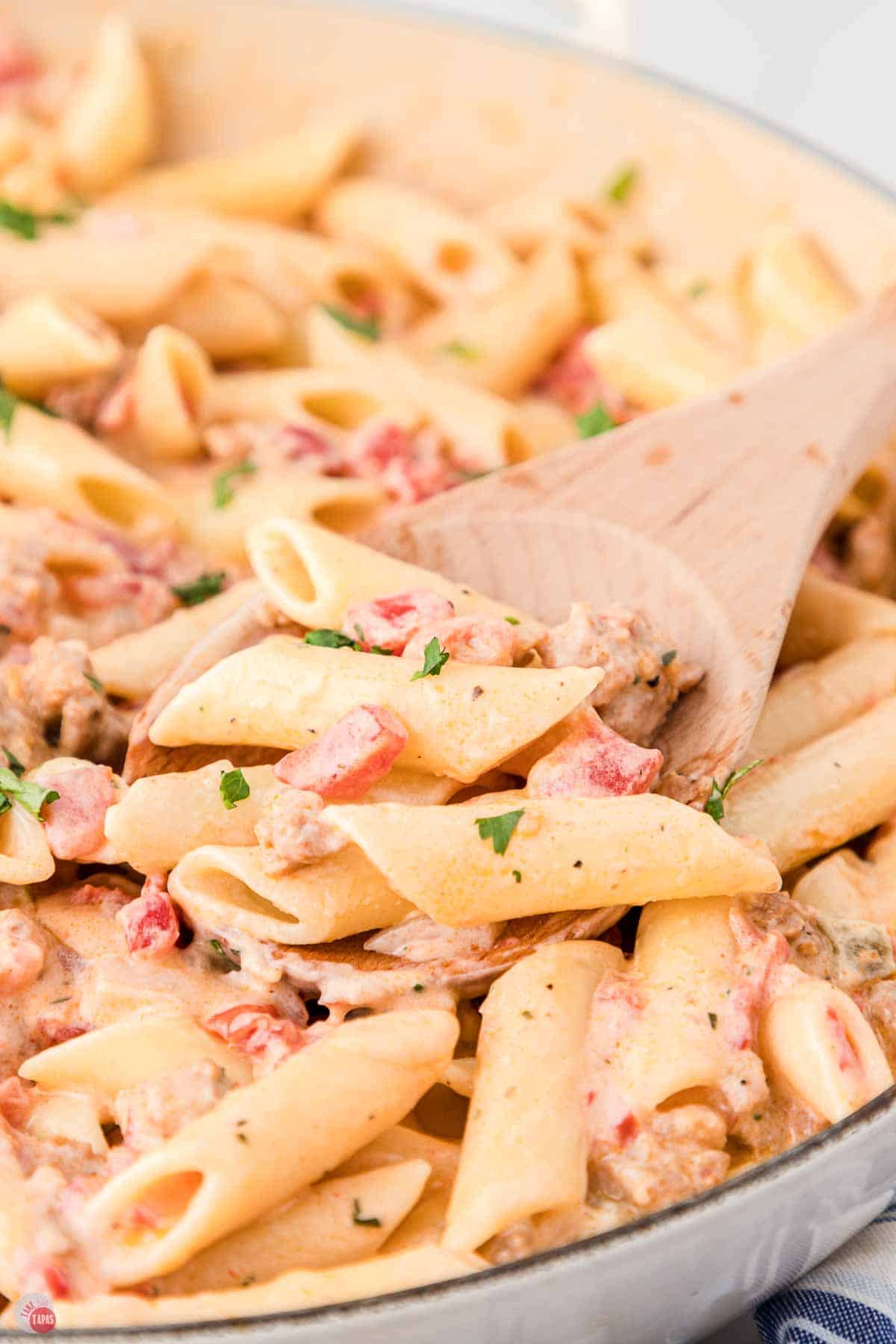 close up of penne pasta and sauce being stirred with a wood spoon
