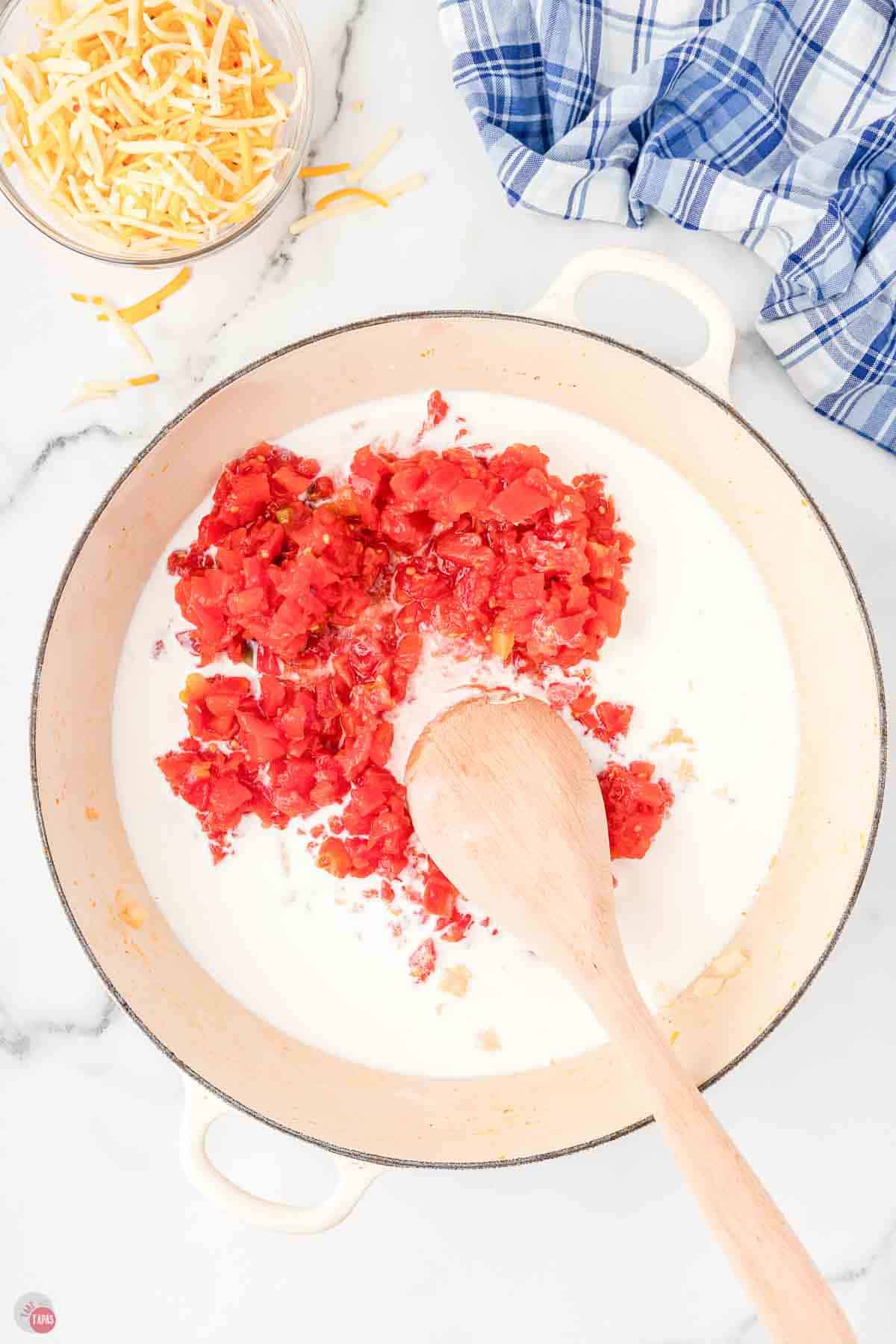skillet with cream and tomatoes being stirred with a spoon