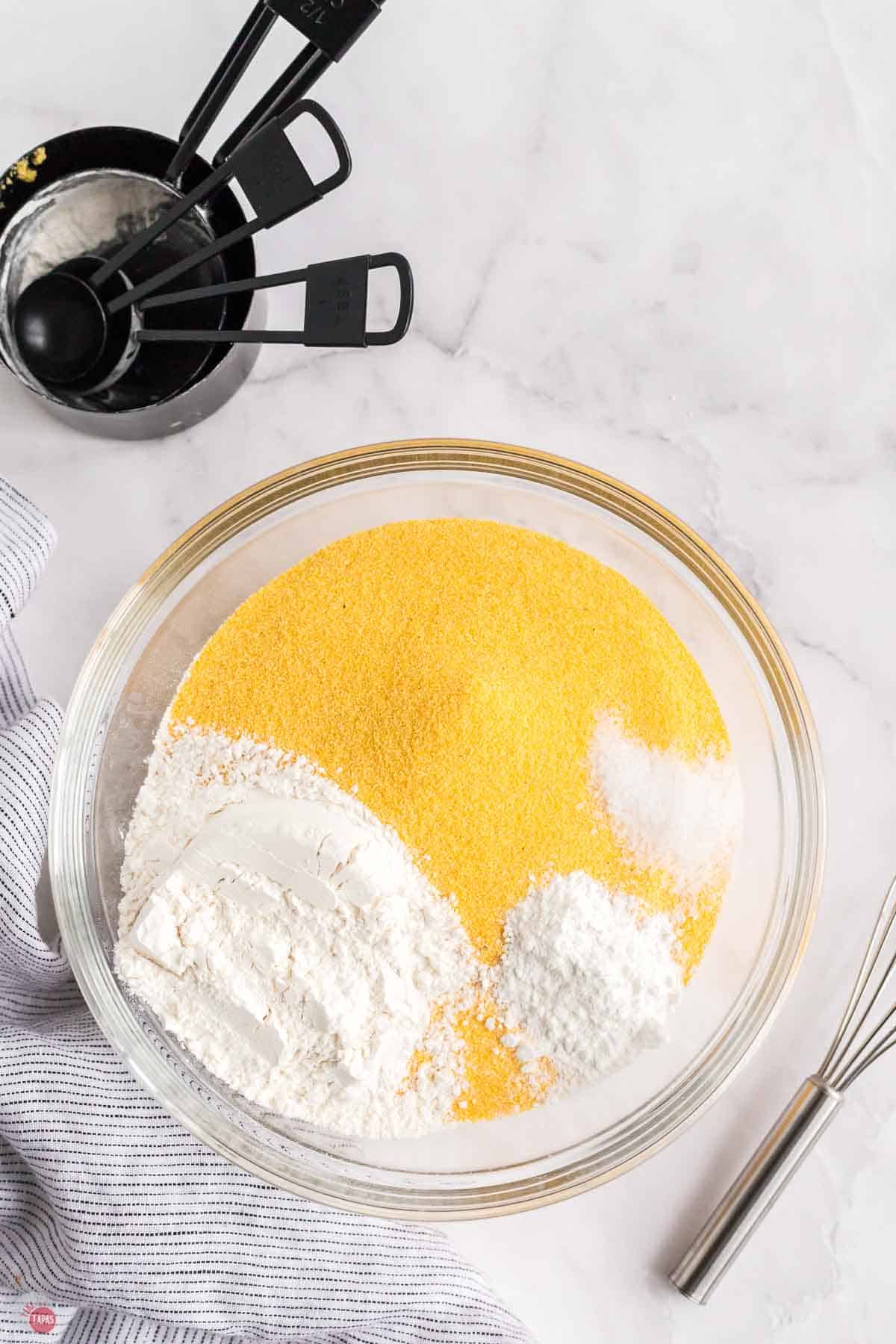 clear bowl of yellow and white powders with a stack of black measuring cups