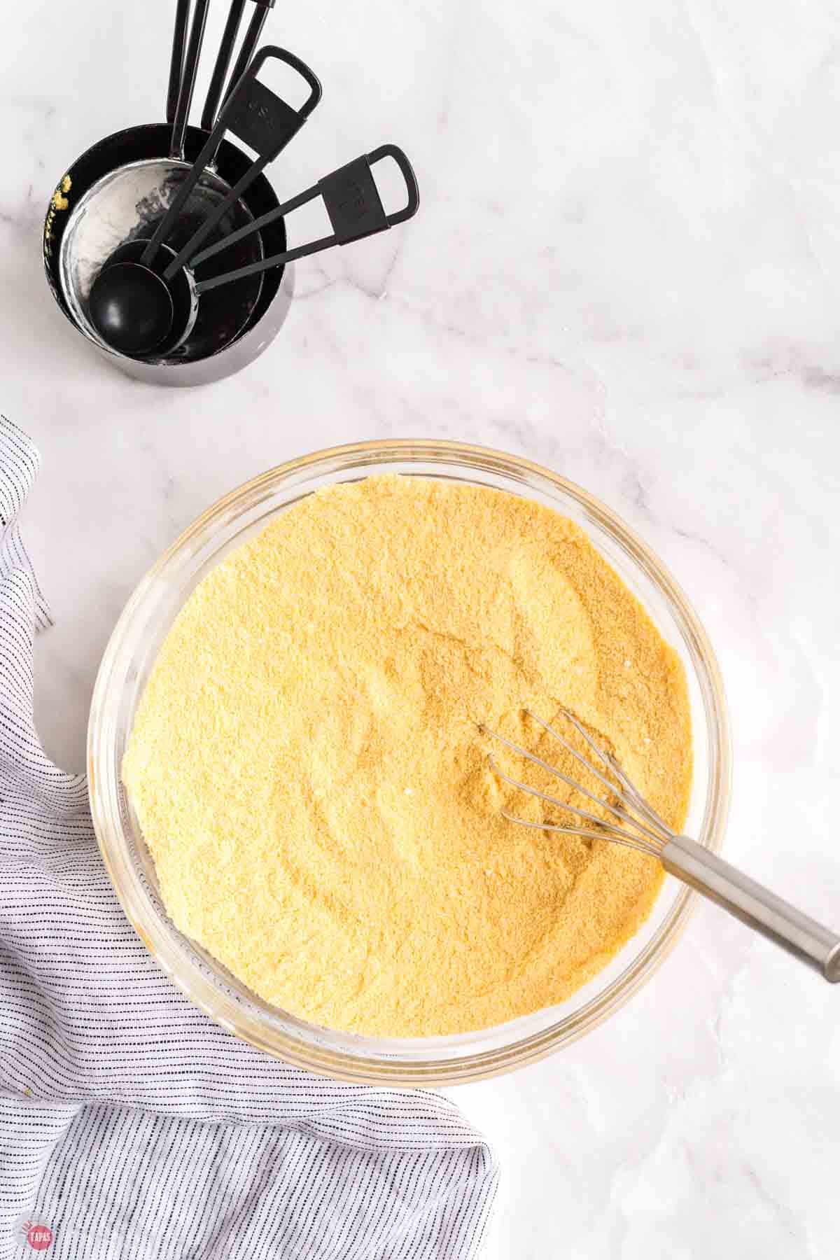 clear bowl of cornmeal being mixed with a wire whisk