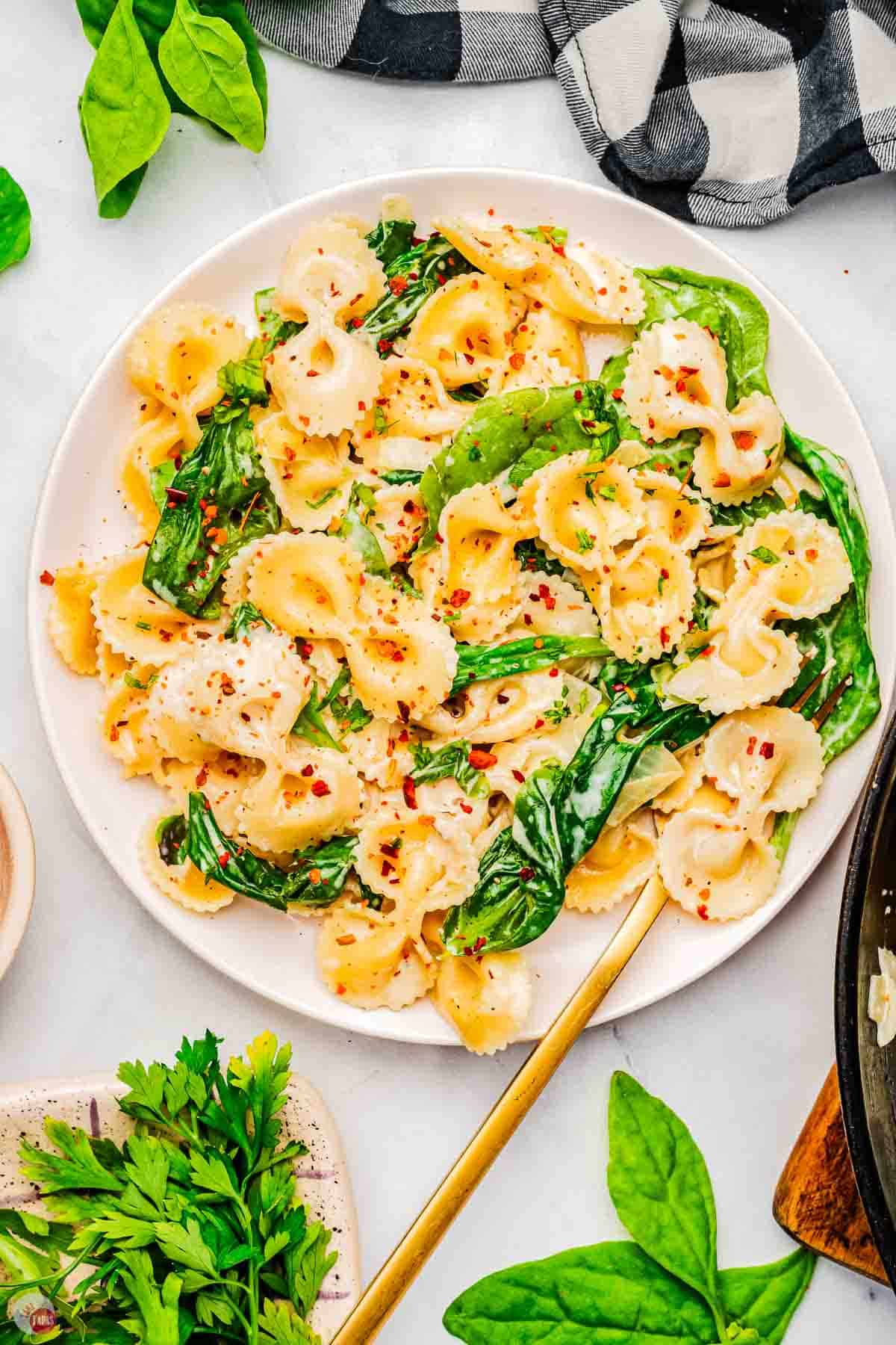 white plate topped with pasta and spinach with a gold fork