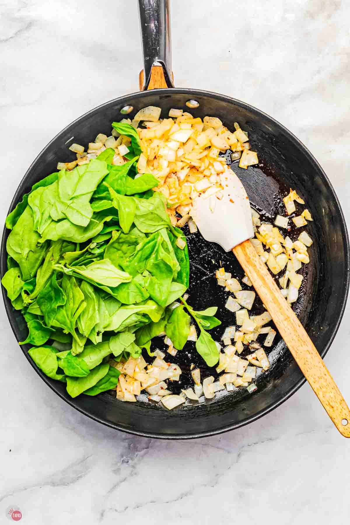 skillet with onion, garlic, and spinach leaves cooking