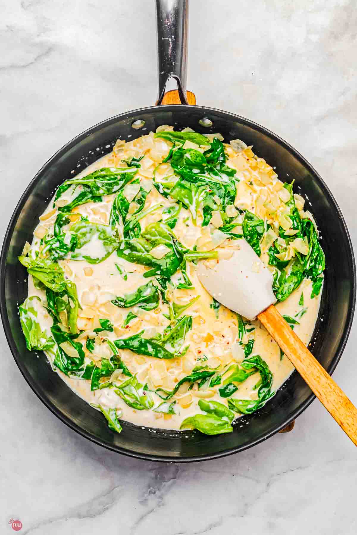 skillet with a creamy sauce and spinach being stirred with a white spatula