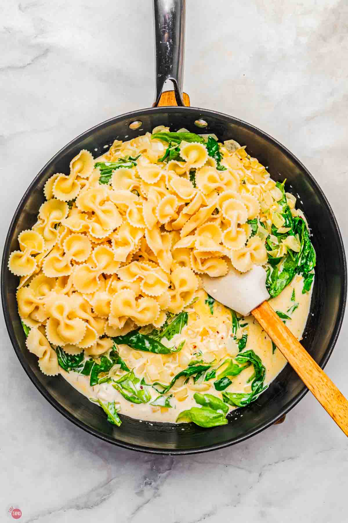 skillet with creamy spinach sauce topped with fresh cooked pasta