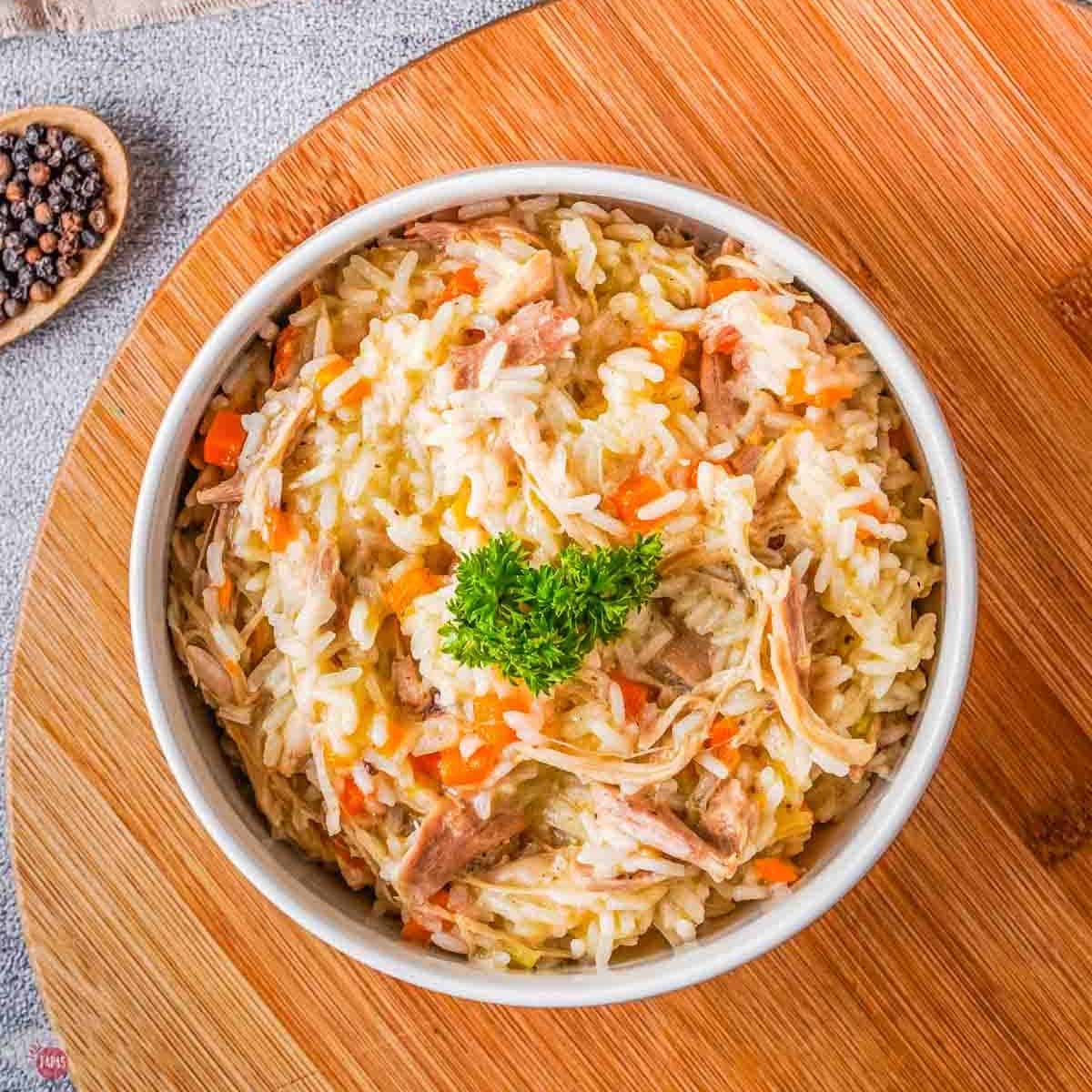 bowl of chicken and rice topped with parsley on a wood board