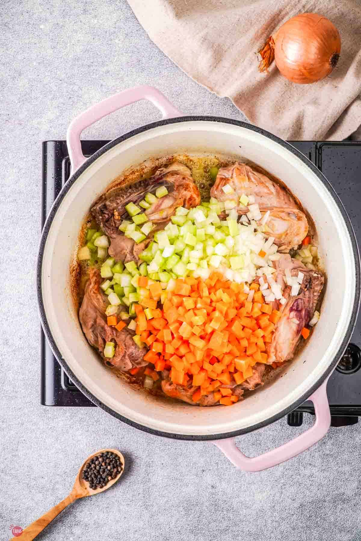 white dutch oven with seared chicken thighs and chopped carrots and celery