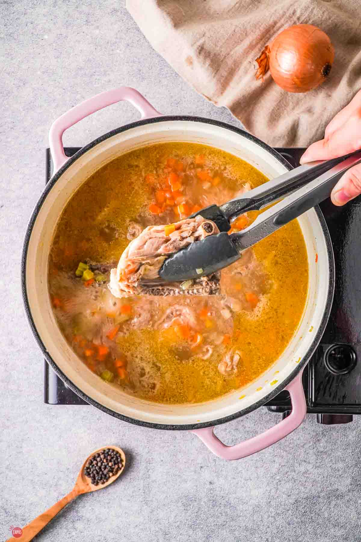 pot of broth with a pair of tongs holding cooked chicken