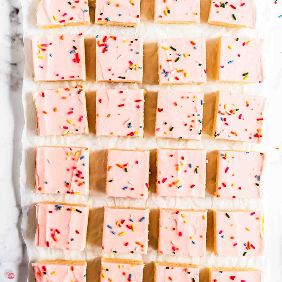 pink frosted sugar cookie bars cut into pieces and placed in rows on a piece of parchment paper