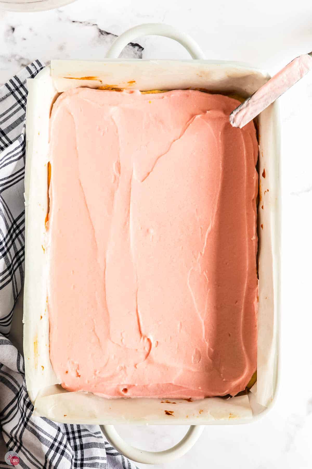 sugar cookie bars topped with pink frosting in a 9x12 white baking dish