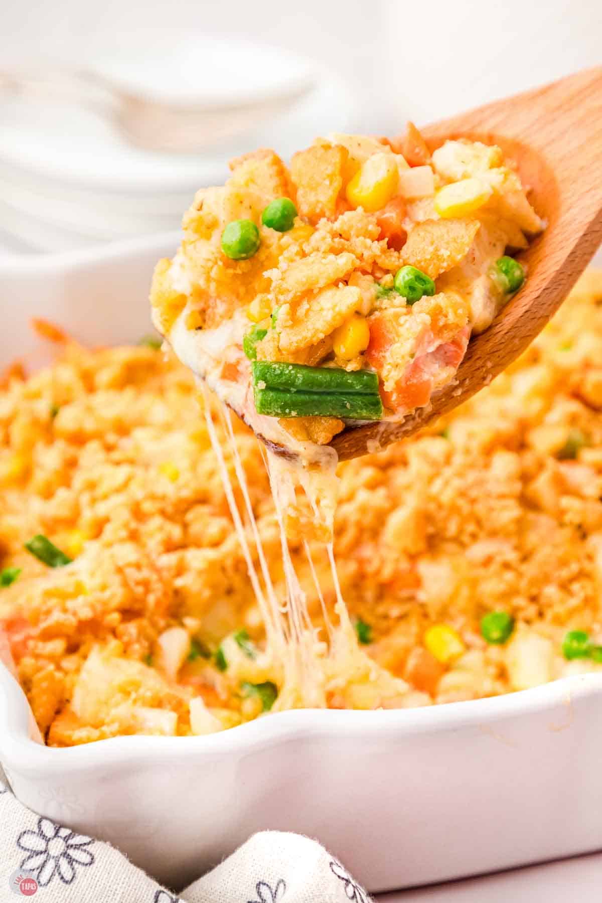wood spoon scooping veg all casserole out of a white dish