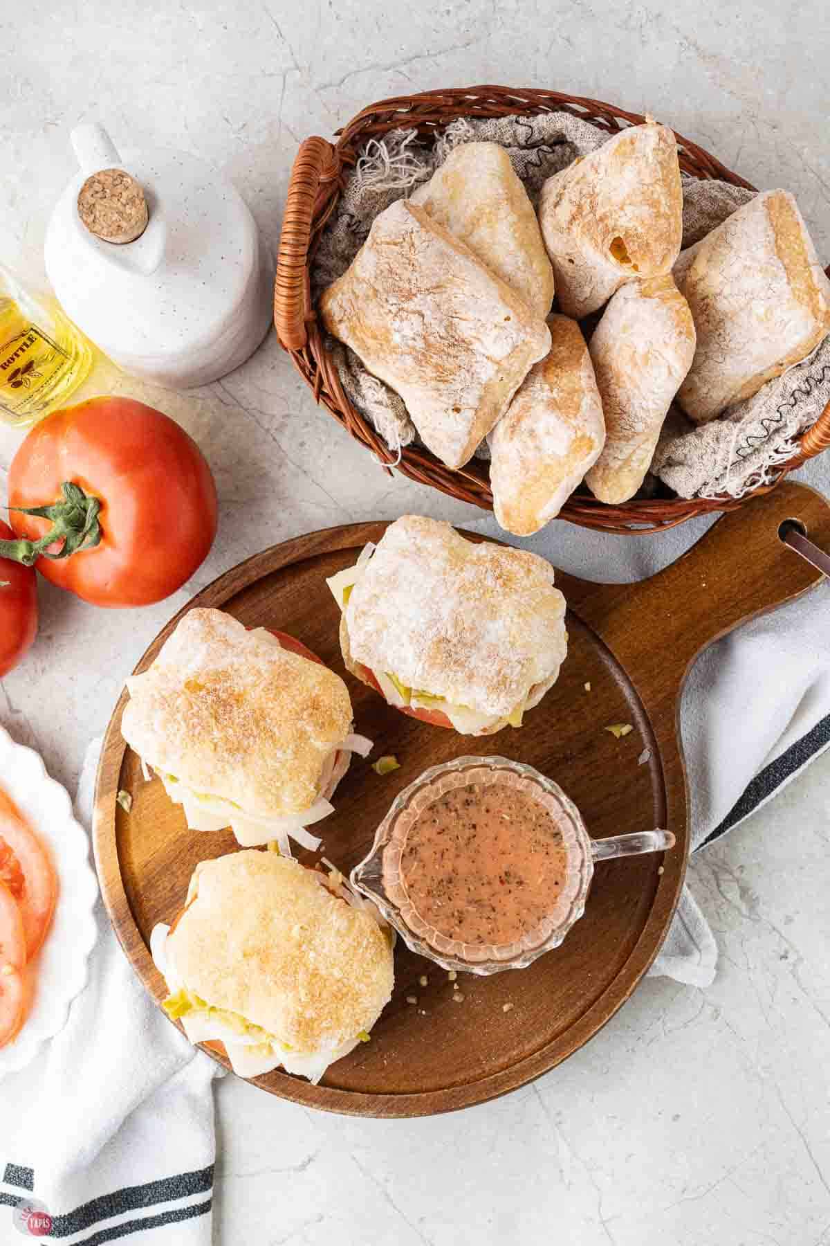 vegetarian sliders, wrapped in parchment paper, on a wood board with a small bowl of salad dressing