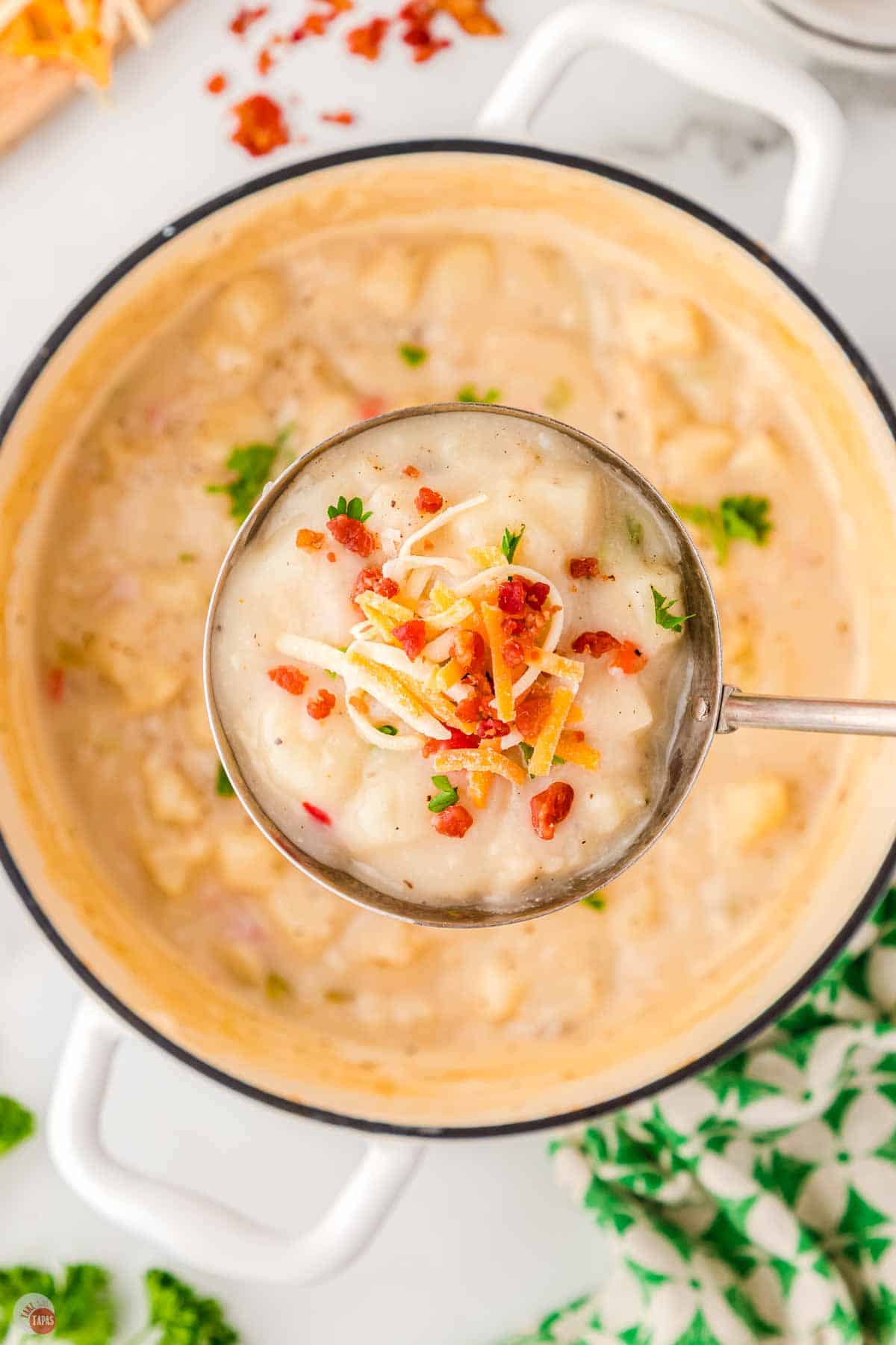 close up of potato soup in a ladle topped with shredded cheese and bacon