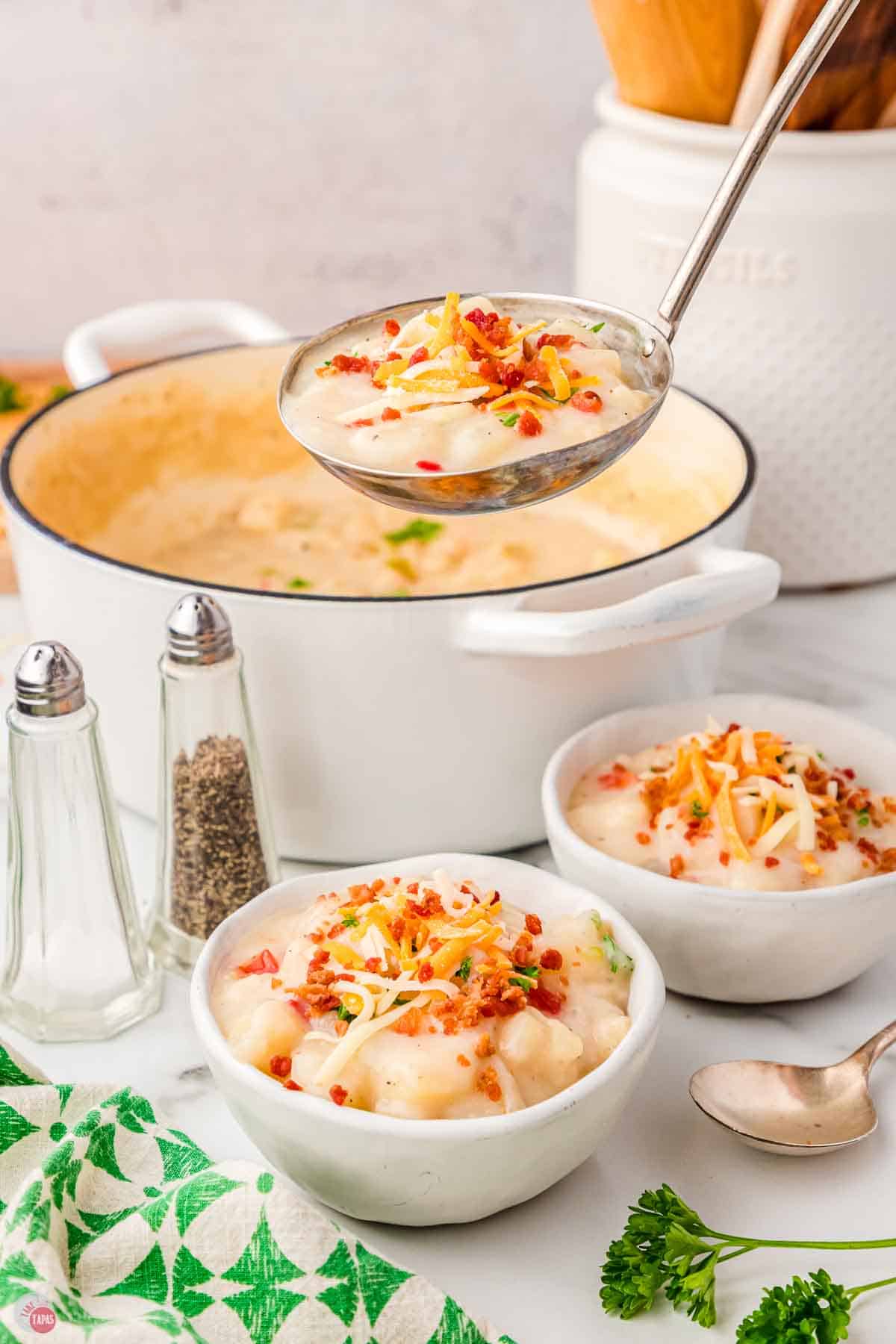 two bowls of soup next to a pot with a ladle scooping some out