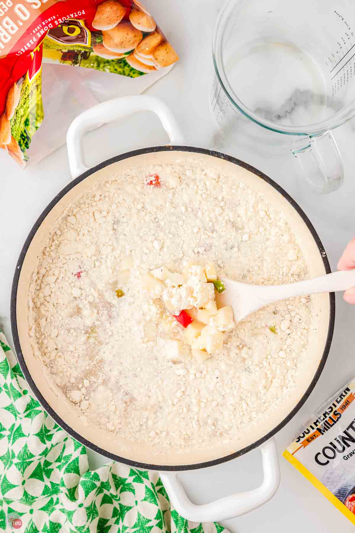 potato soup being stirred with a white spoon in a white pot