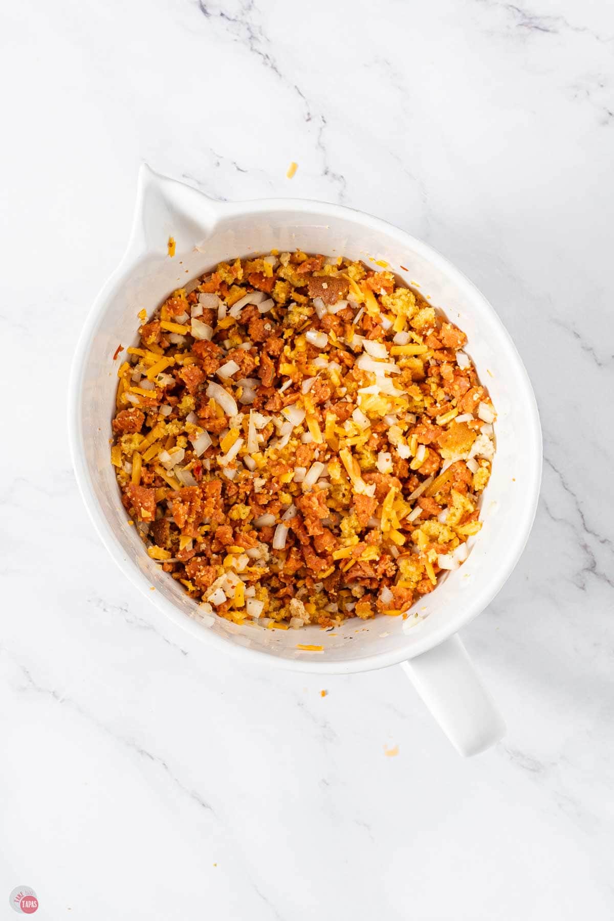 white mixing bowl with cornbread stuffing mix, cheese, and cooked sausage