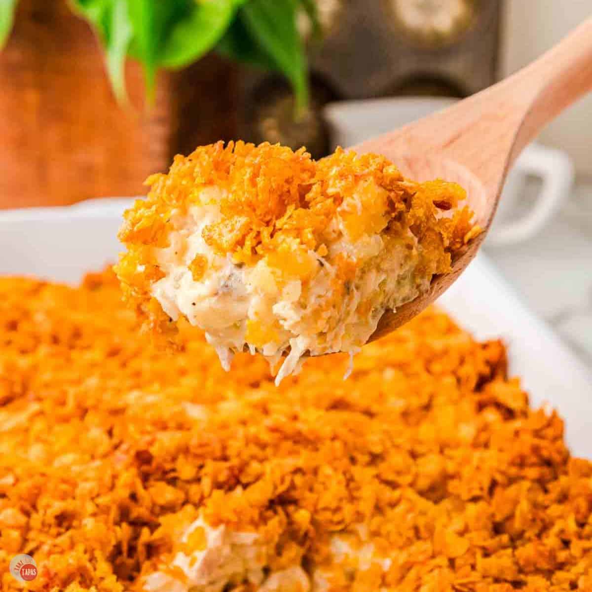 scoop of casserole with cornflake topping with wood spoon and white dish