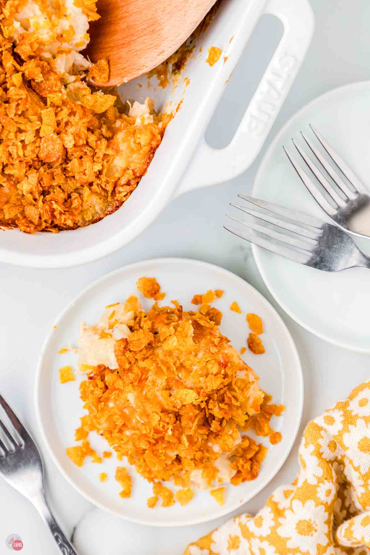 plate of casserole next to a stack of plates and forks and a baking dish