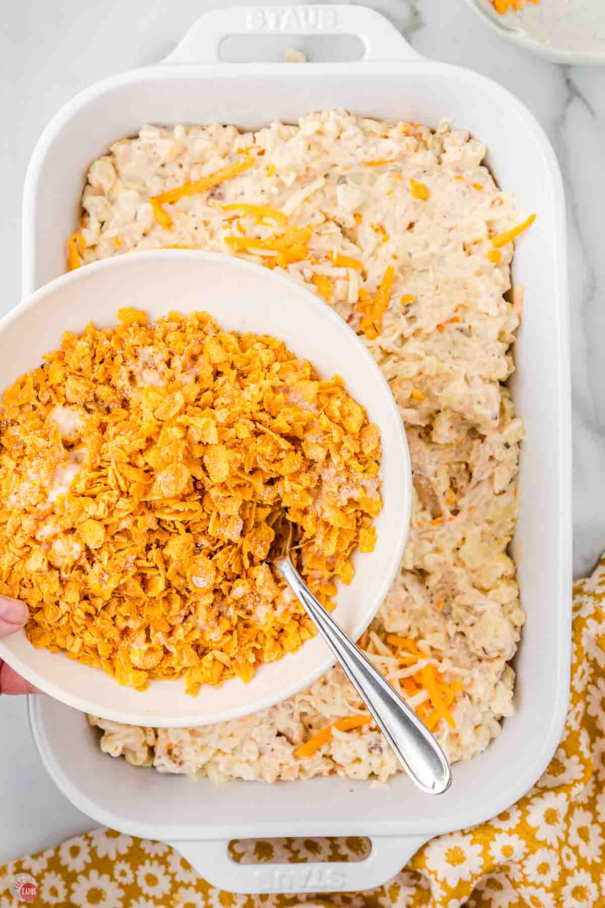 bowl of cornflake topping being spread over a chicken mixture