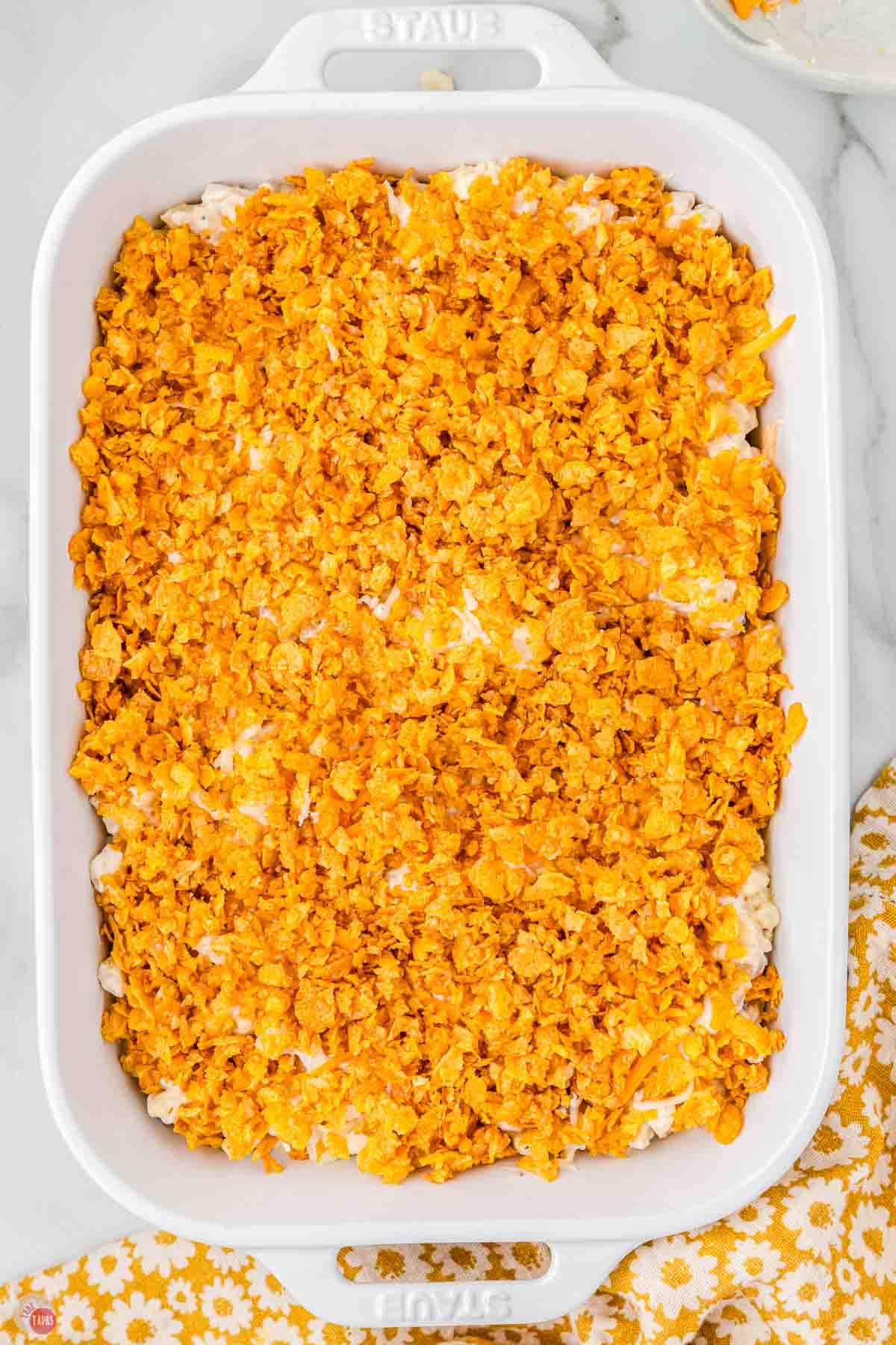 unbaked casserole in a white dish with a cornflake topping