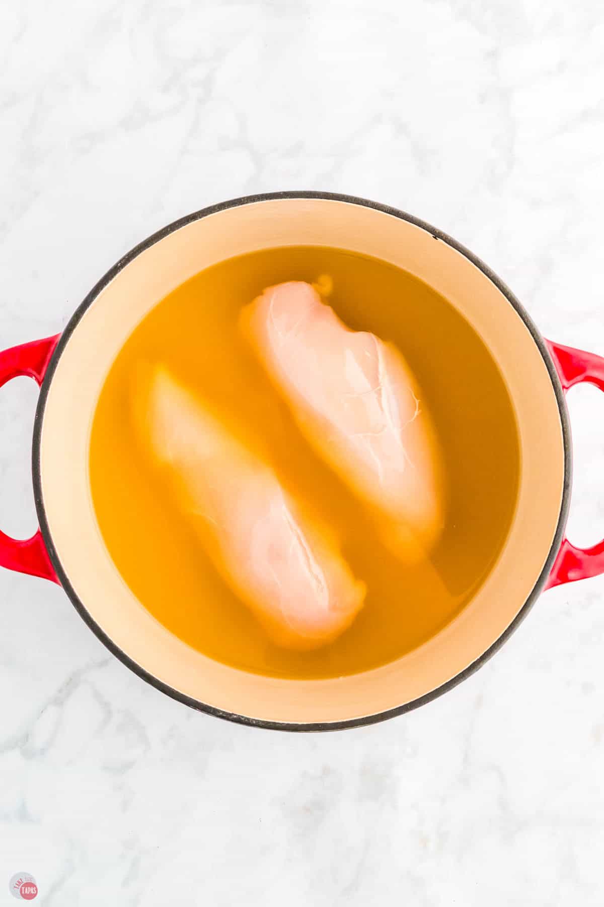 two chicken breasts simmering in a pot of broth
