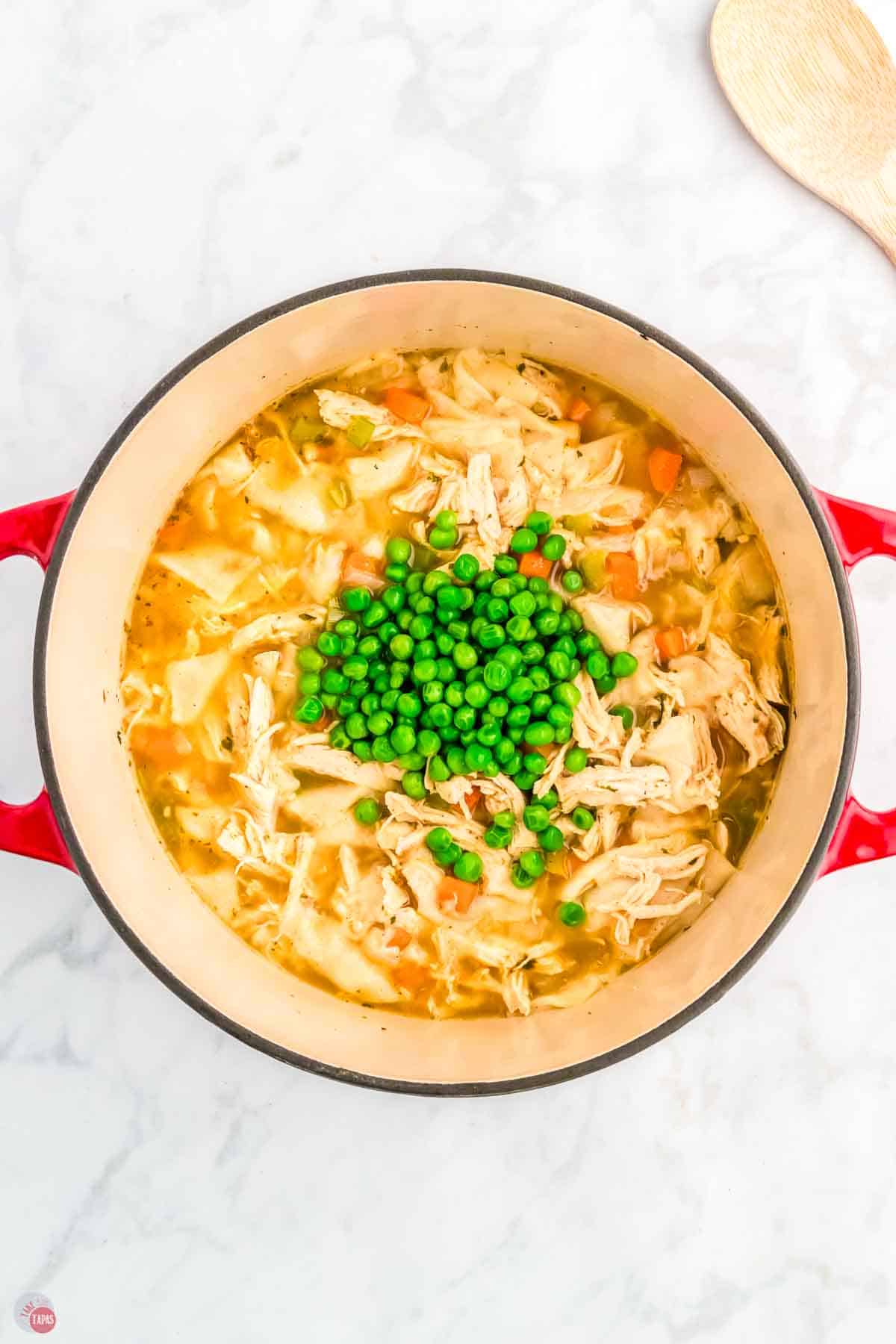 red pot of chicken soup with green peas on top