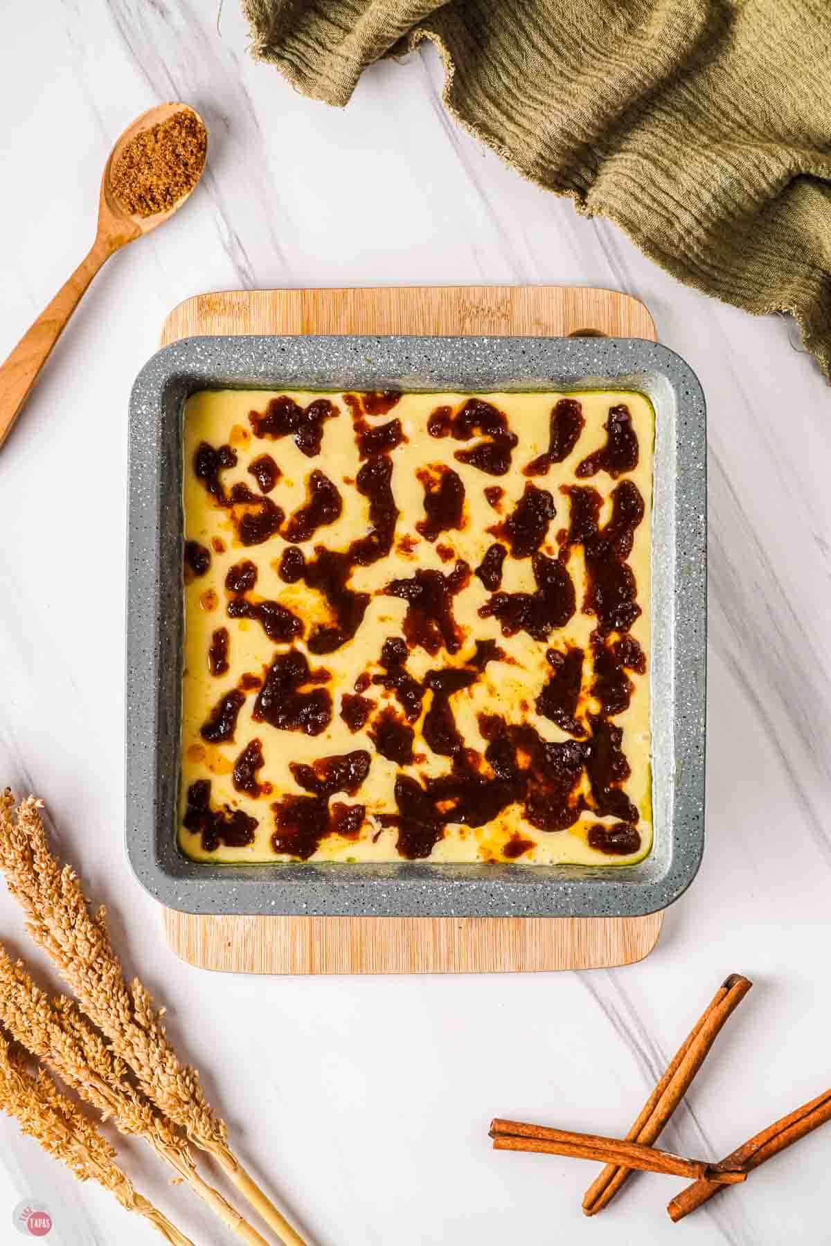 square baking pan filled with cake batter and topped with cinnamon swirl