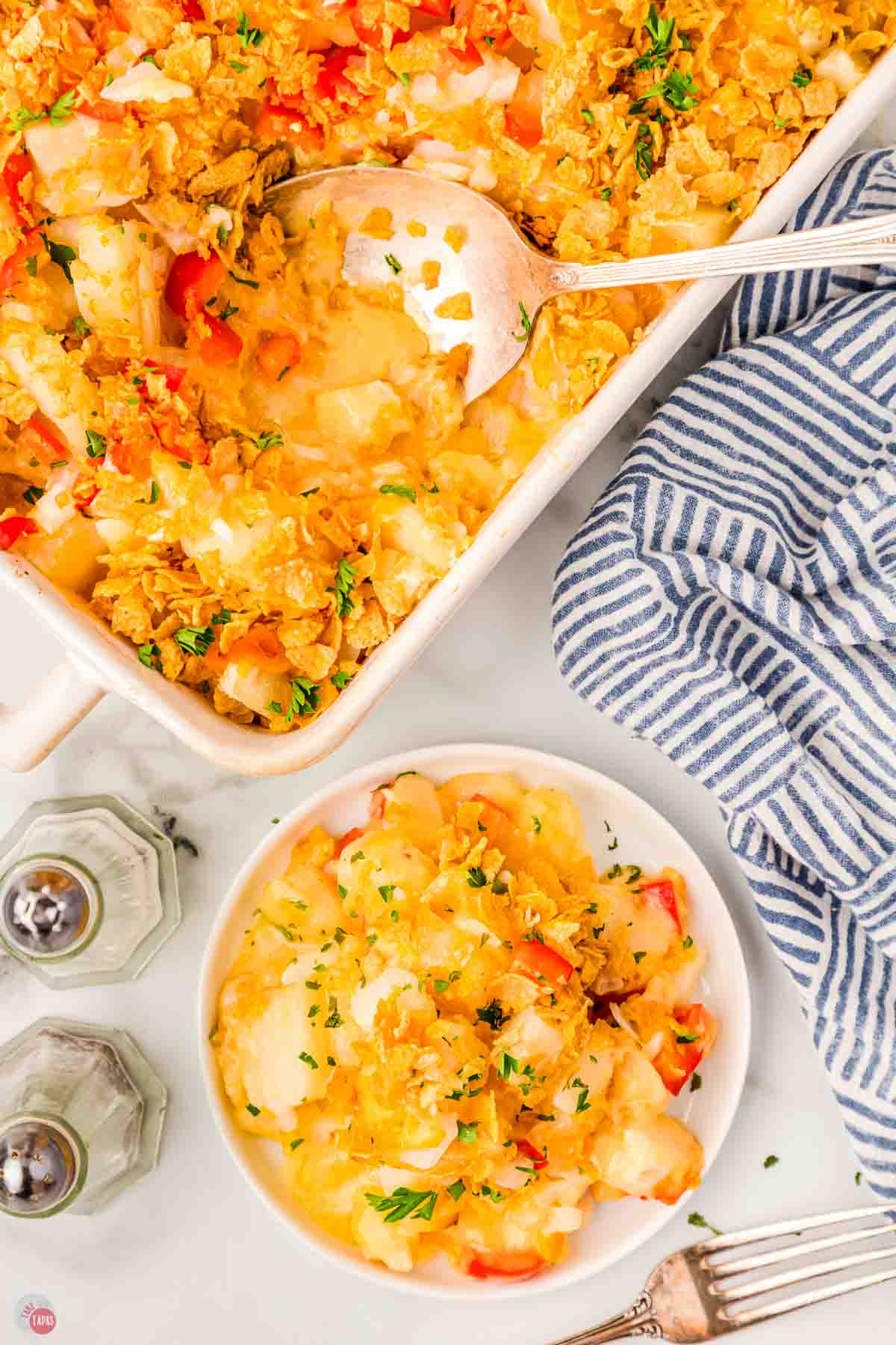 dish of cottage potatoes with a scoop on a small white plate next to salt and pepper shakers