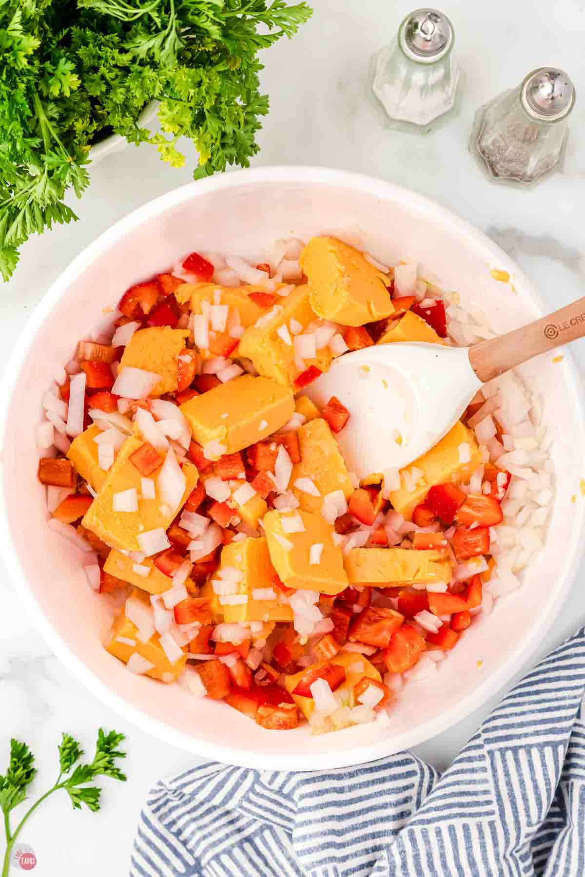 white mixing bowl full of onions, bell peppers, and cubes of Velveeta cheese