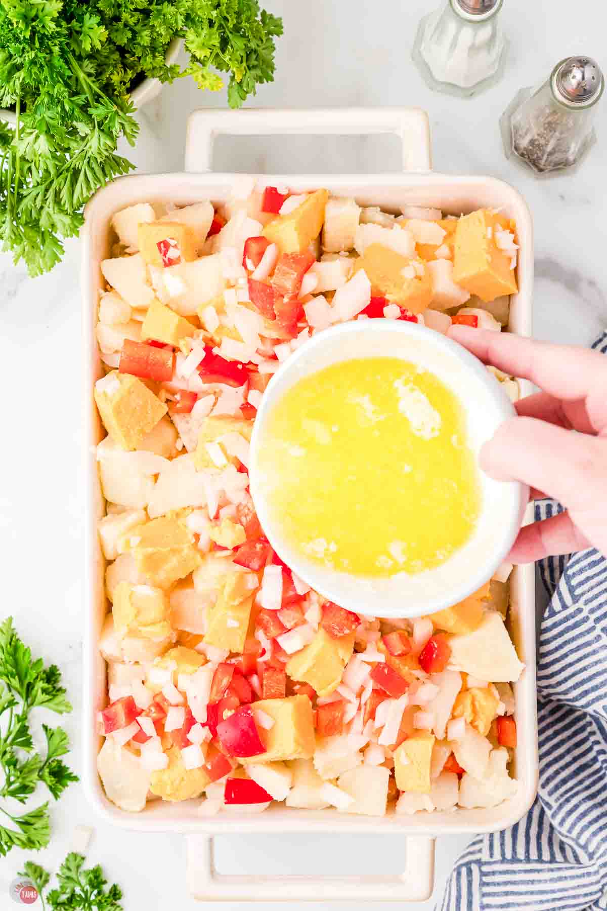 potato casserole in a baking dish with a bowl of melted butter being poured on top