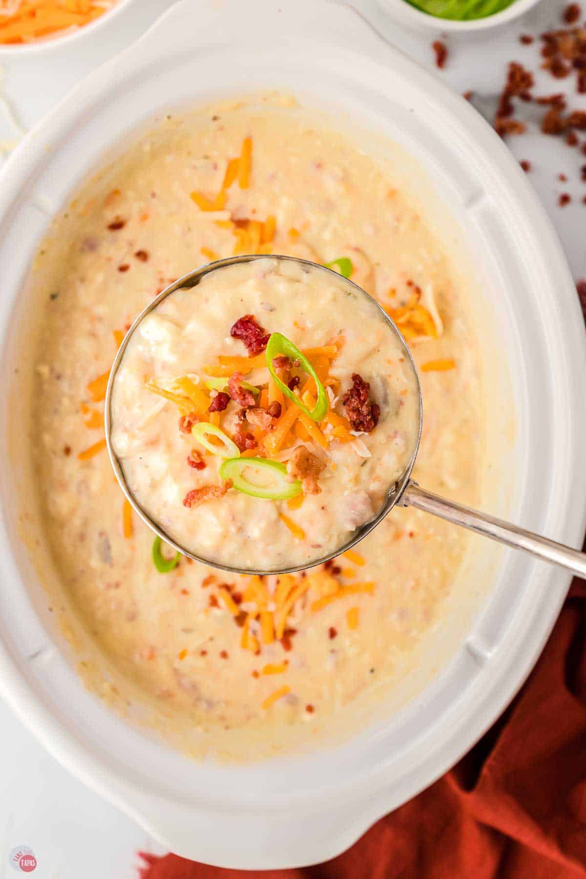 close up of ladle filled with potato soup and topped with cheese and bacon